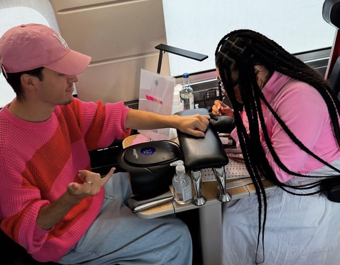 Une femme en train de se faire tatouer par une artiste dans une cabine de tatouage, avec un homme assis à côté.