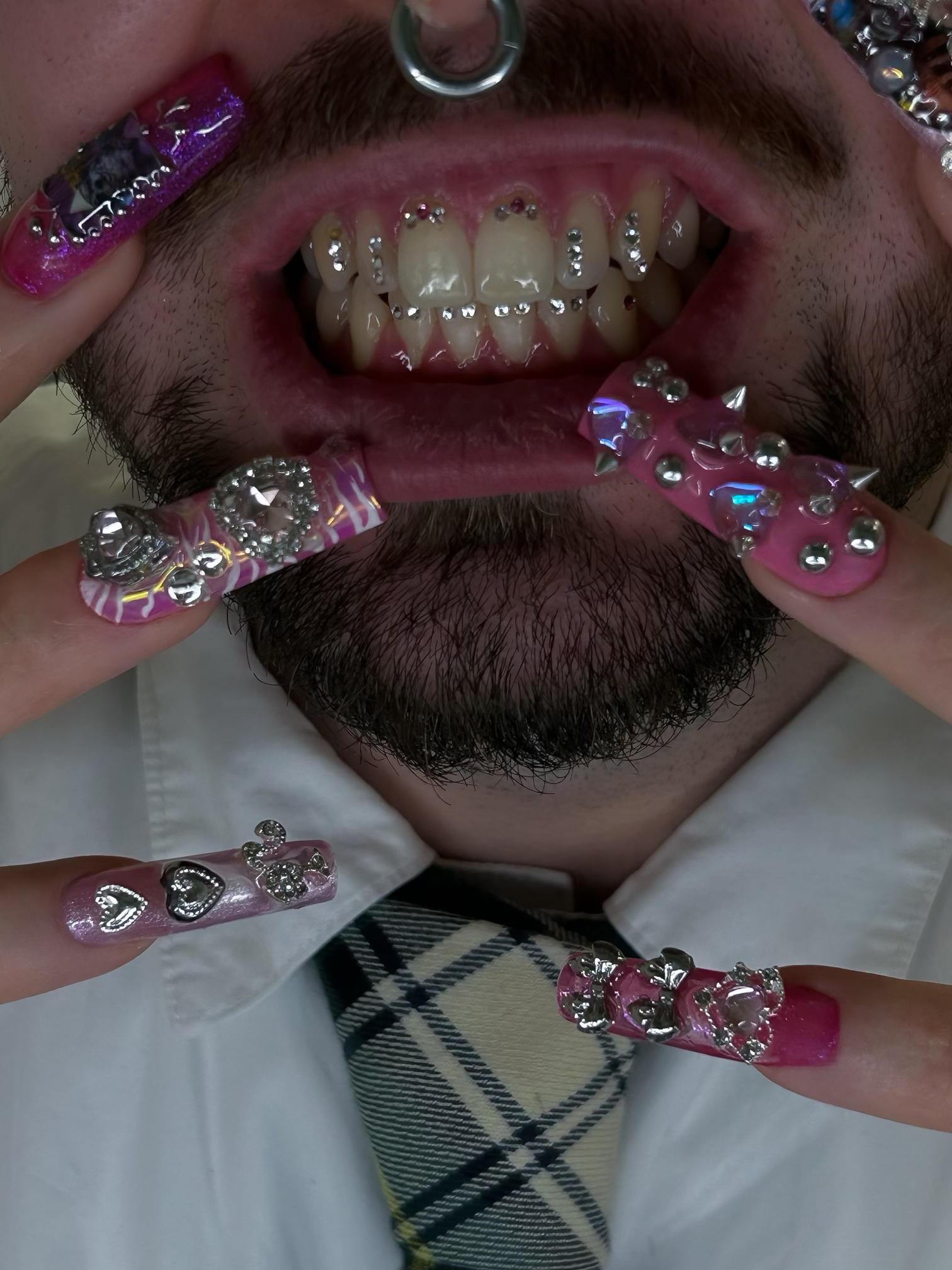Homme avec un tatouage numérique et des bijoux sur les doigts, montrant ses dents avec des bijoux dentaires en diamants.