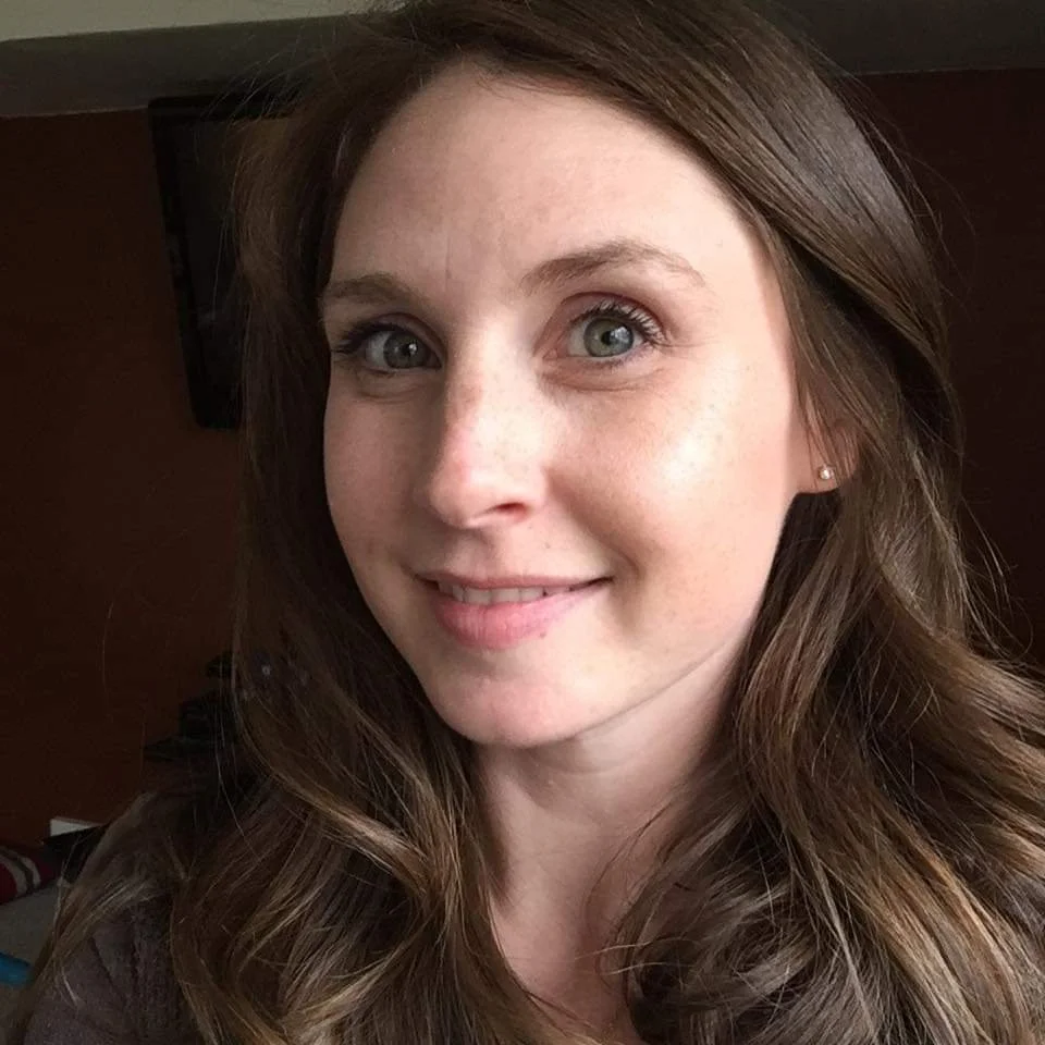 A woman with wavy brown hair and blue eyes smiling indoors.
