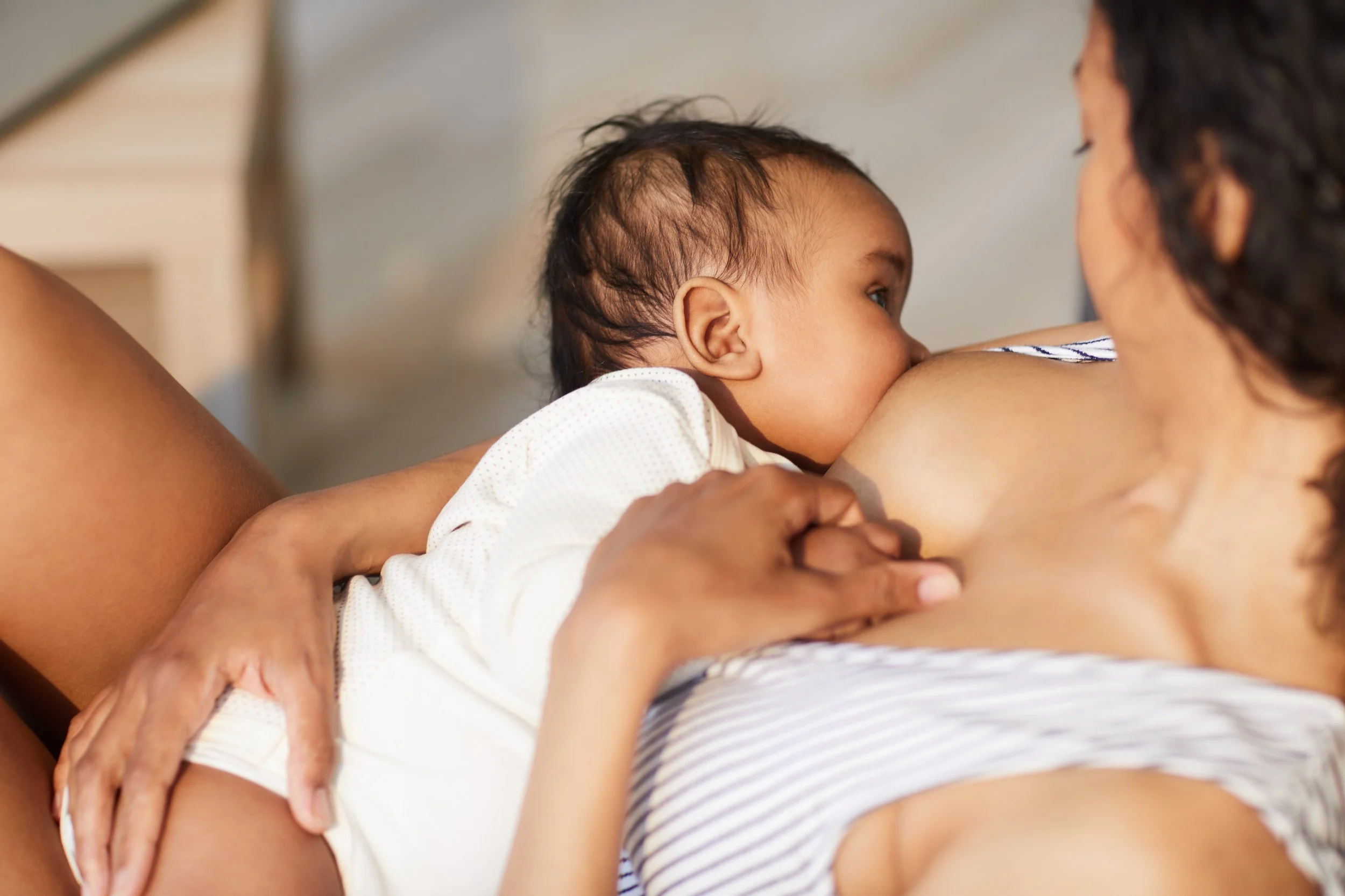 A baby breastfeeding from a woman, with the woman's hand supporting the baby's head.