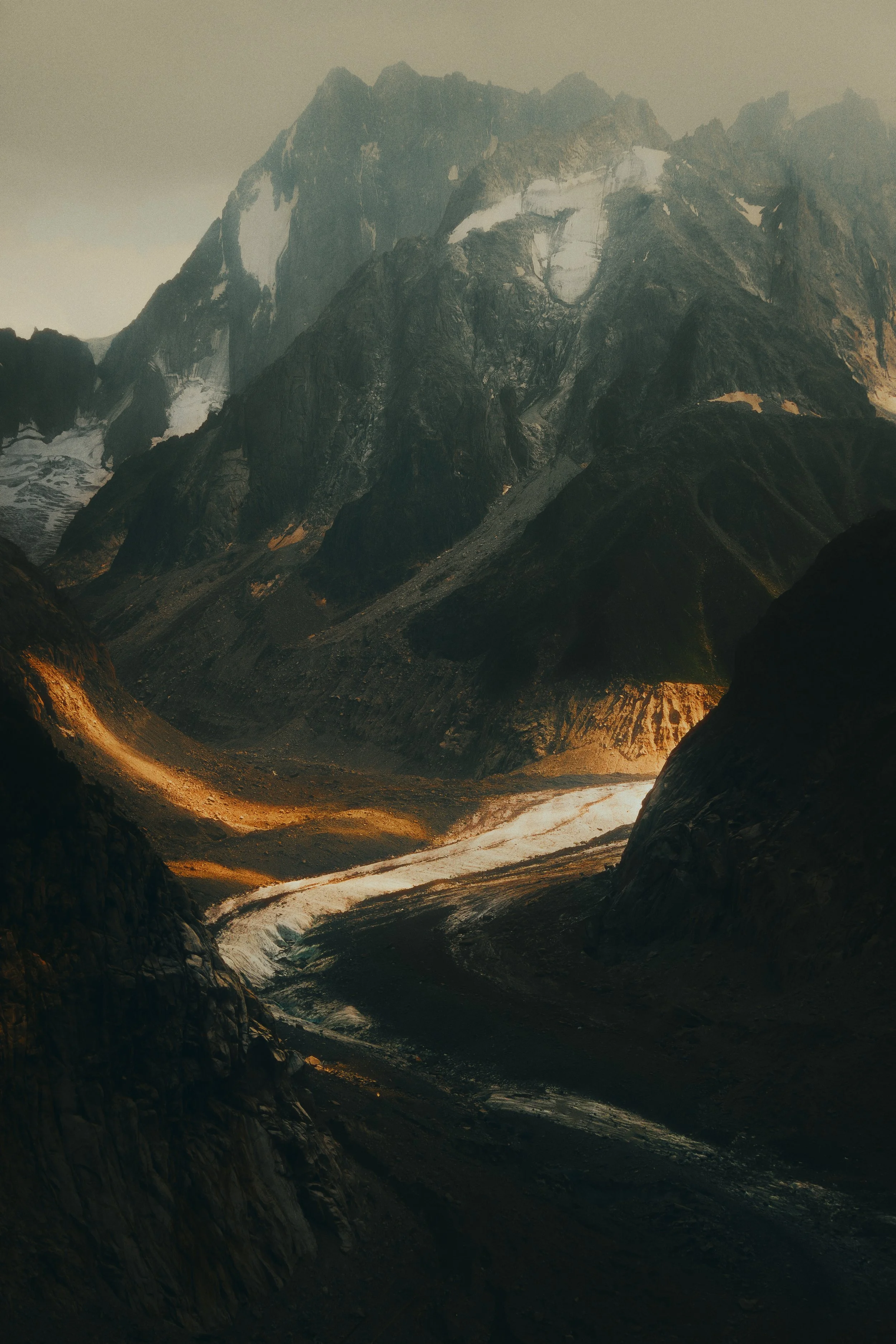 Montagnes rocheuses avec des sommets enneigés et une vallée avec une rivière serpentant au fond.