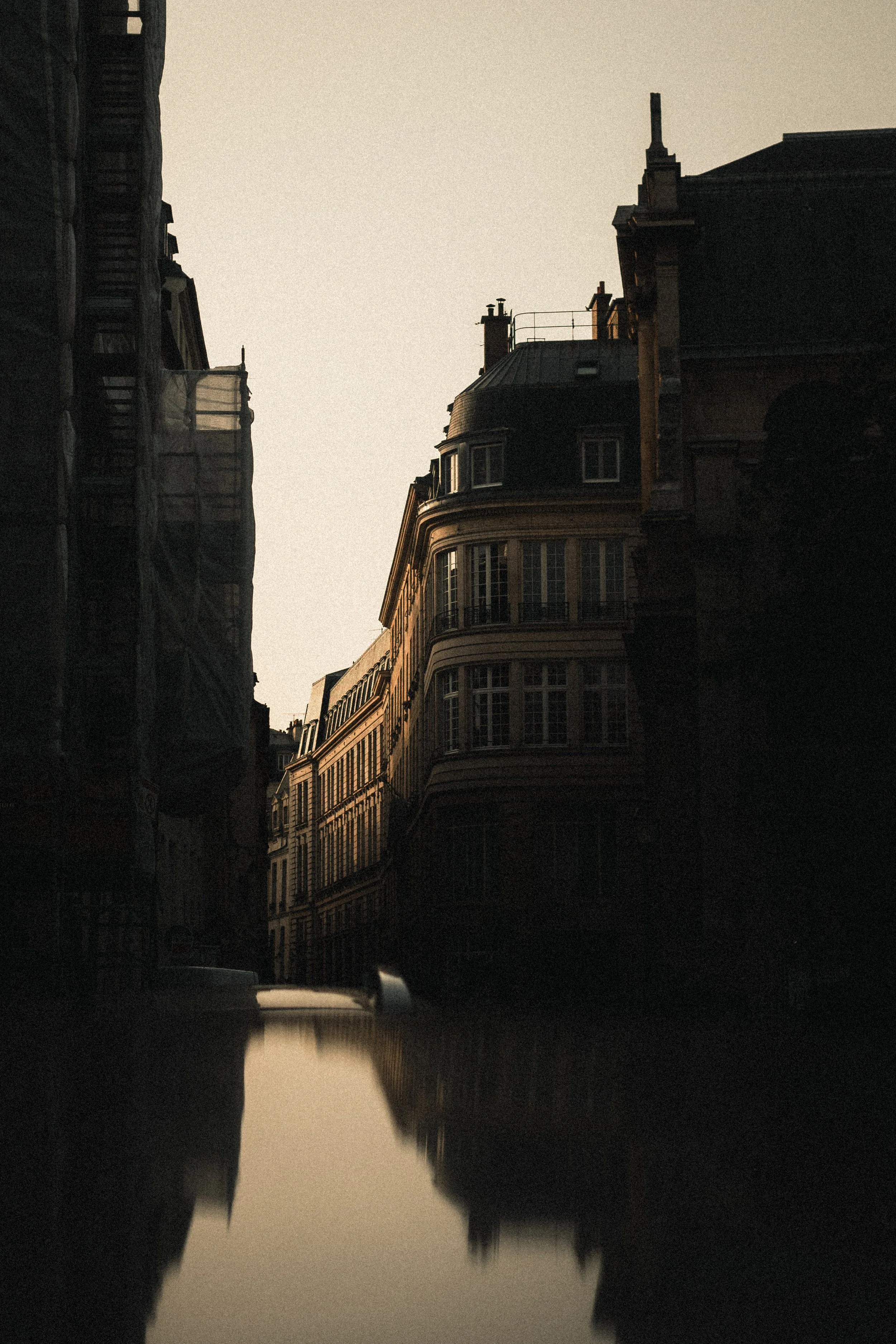 Une vue de bâtiments anciens le long d'une canalisation, avec une lumière tamisée du coucher du soleil et la reflection de la scène dans l'eau.