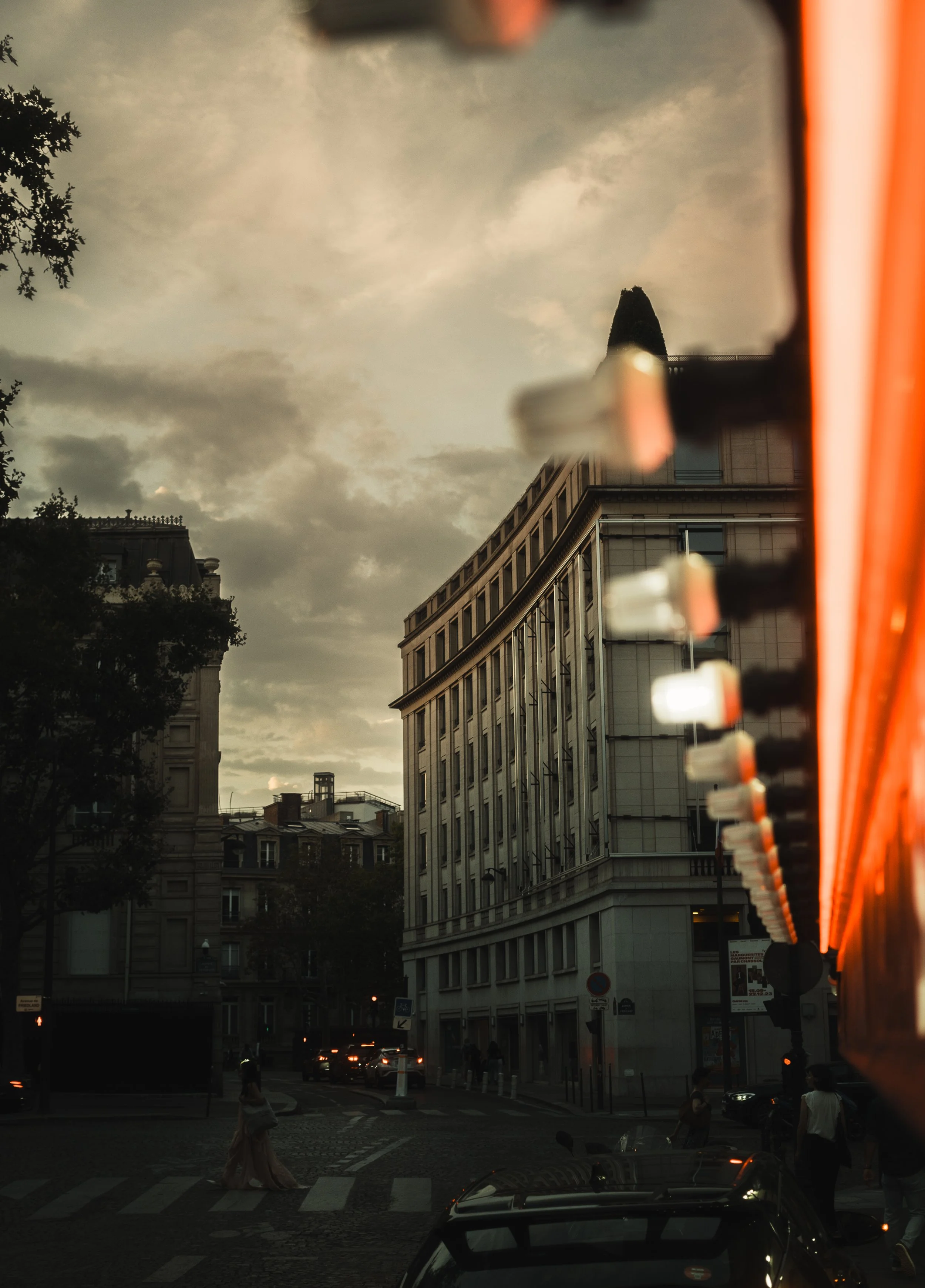 Vue de la ville avec un bâtiment moderne, une rue avec des voitures et des piétons au coucher du soleil, vue à travers une surface réfléchissante.