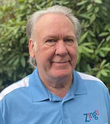 Photo of Zing HQ owner, Jeff Hoerth, standing outside. He is wearing a bright blue polo with white strips on the sleeves and an embroidered Zing HQ logo.