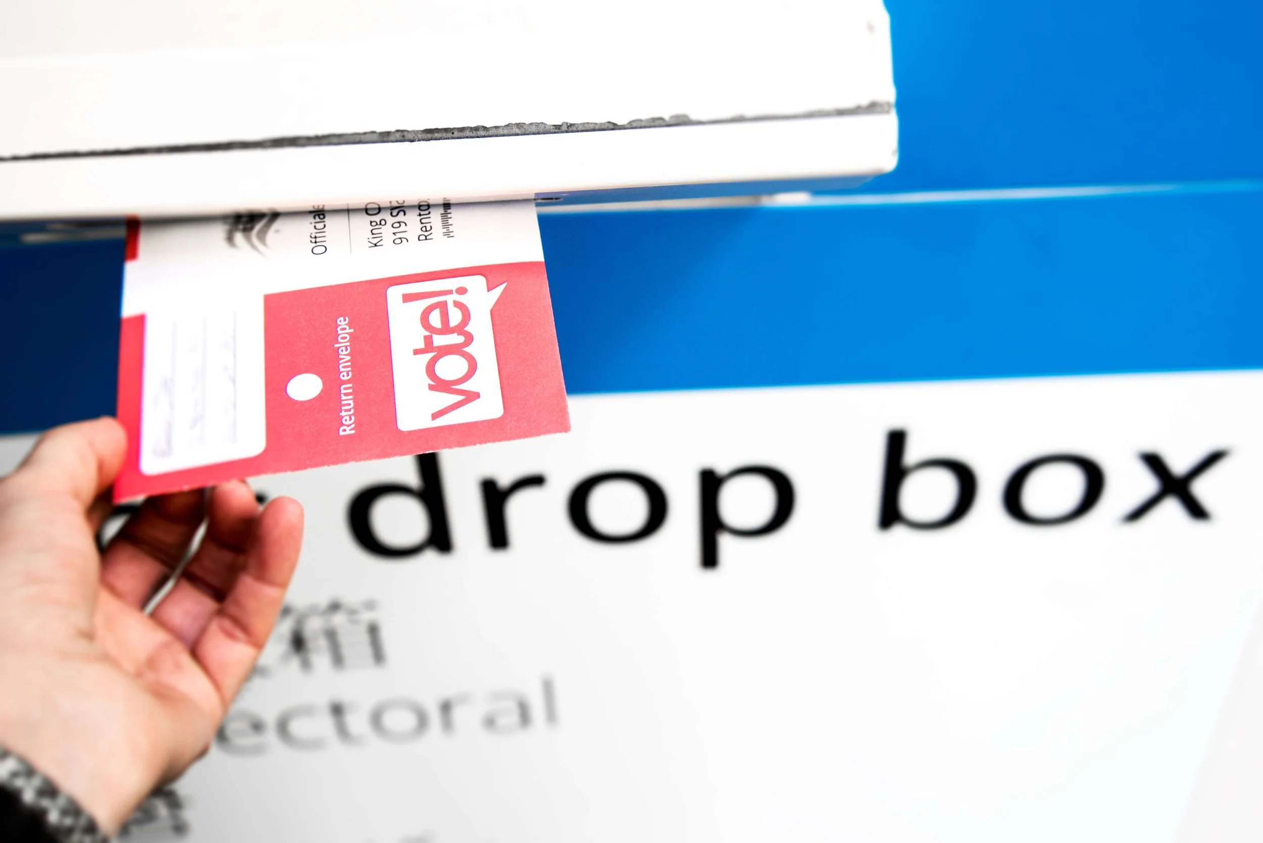 A hand inserting an envelope into a ballot dropbox.