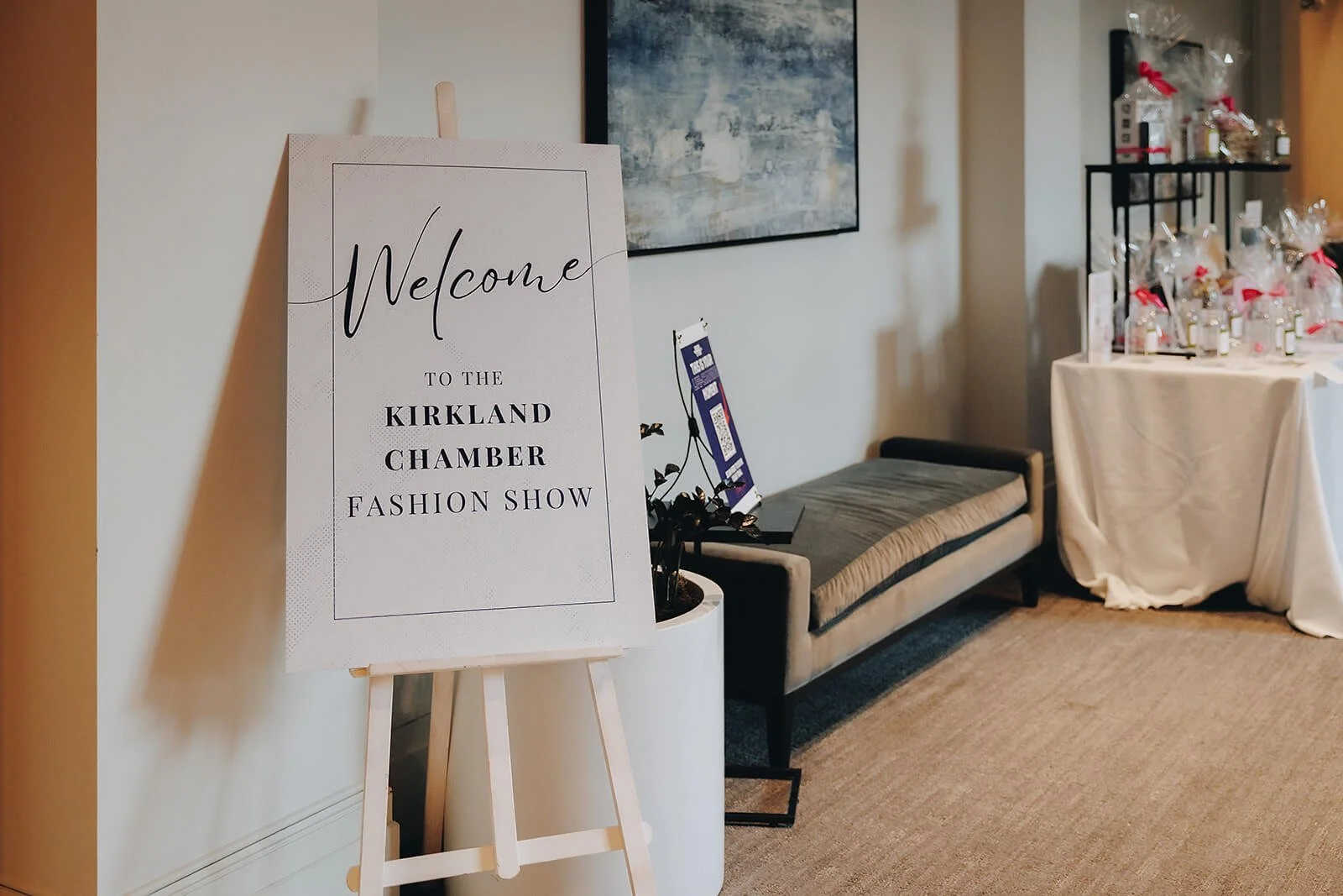 Sign displayed at event that reads "Welcome to the Kirkland Chamber fashion show". The sign is displayed on a wooden easel.