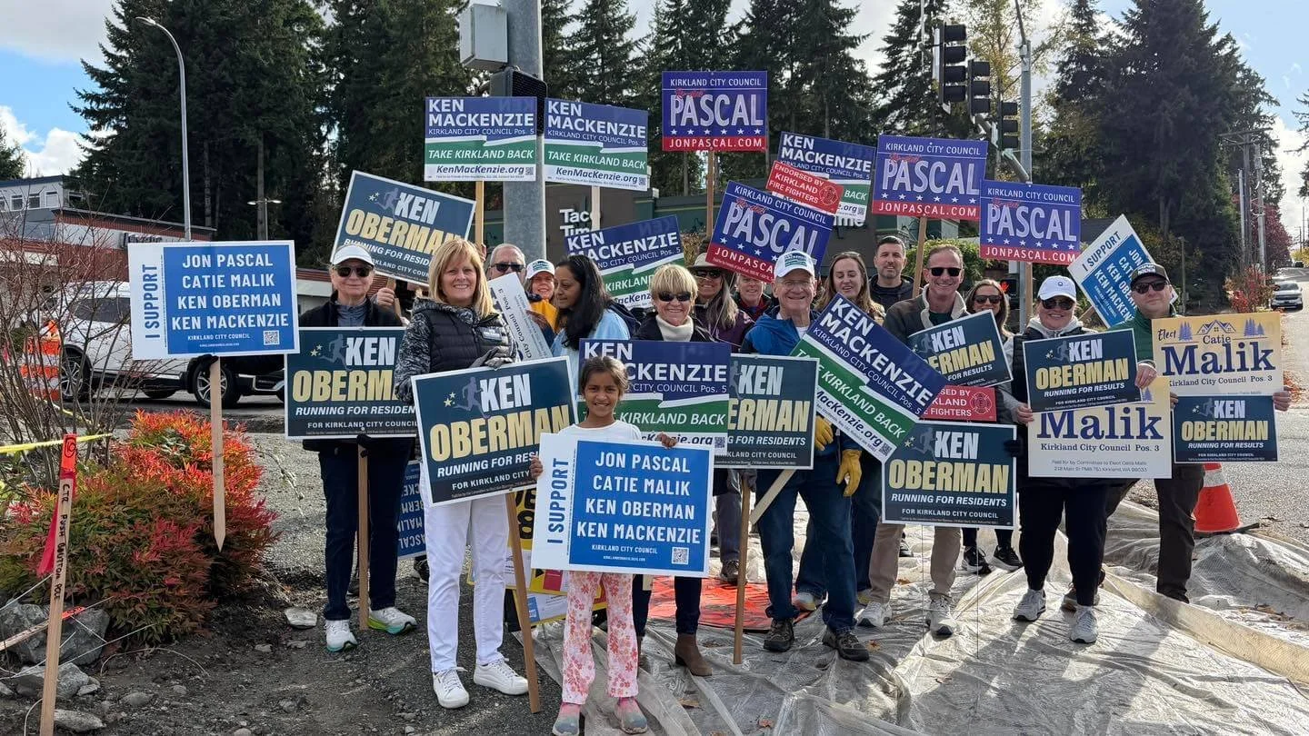 A crowd of people holding up a variety of political campaign signs for different candidates running for Kirkland city council.