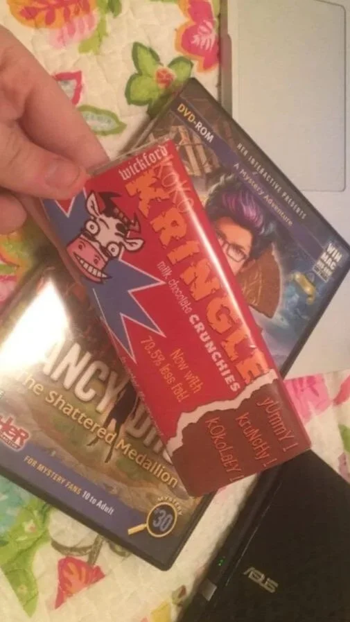 Someone holding a HER Interactive custom branded chocolate bar next to the Nancy Drew computer game case.