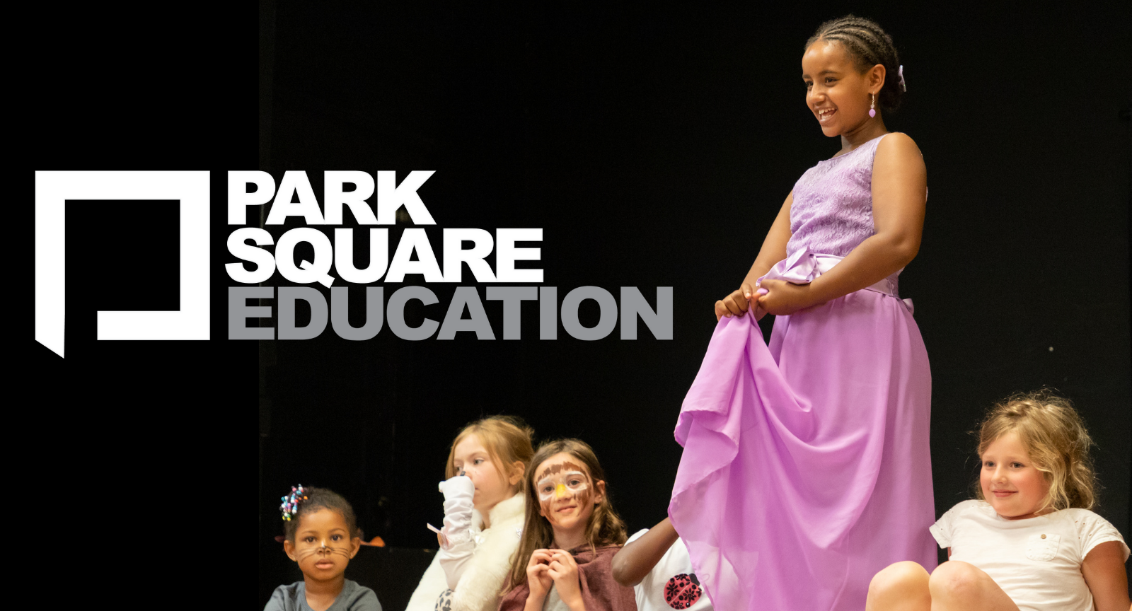 Young girl on stage in a pink dress with four other girls sitting nearby, with 'Park Square Education' logo in the top left corner.