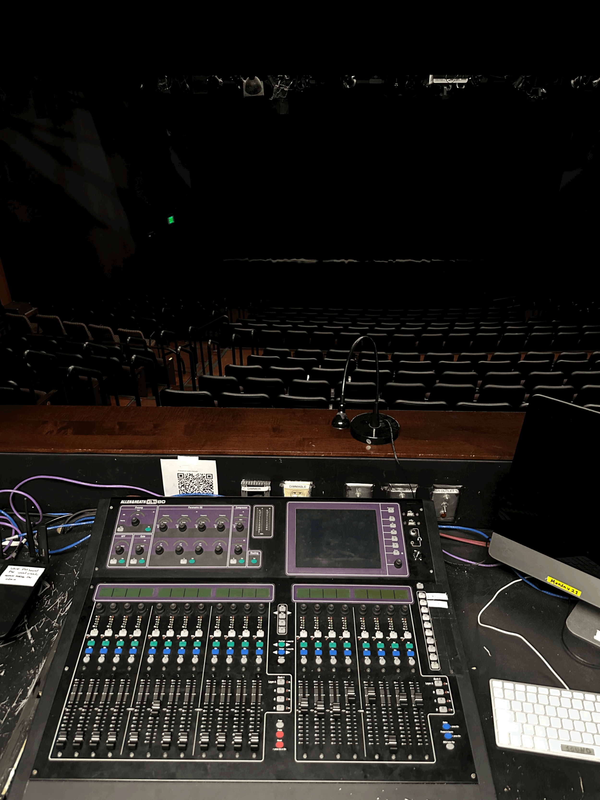 View from the stage overlooking the empty theater with a sound mixing console, microphone, and laptop in the foreground.