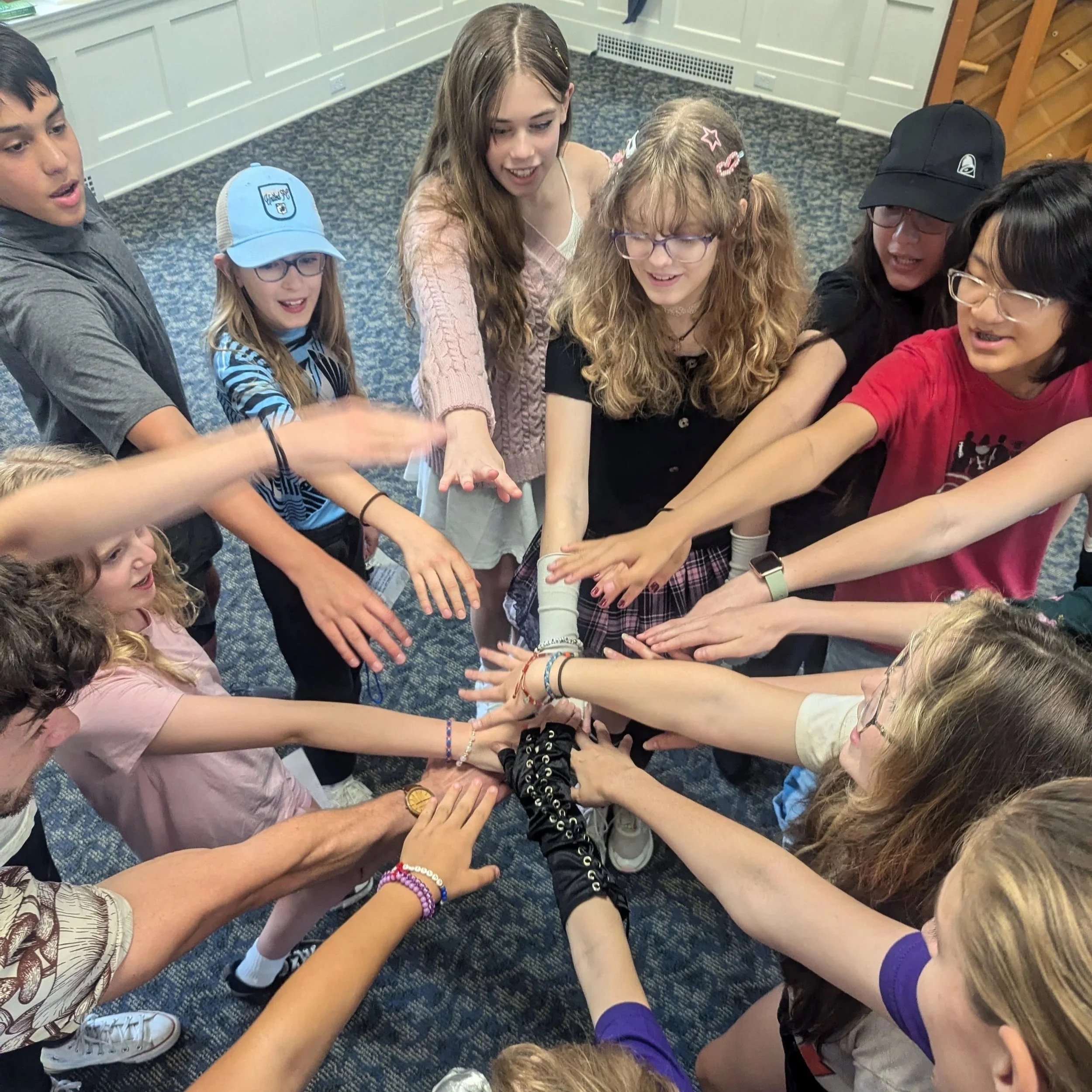 Group of diverse children and teenagers reaching into the center with hands stacked together in a show of unity.