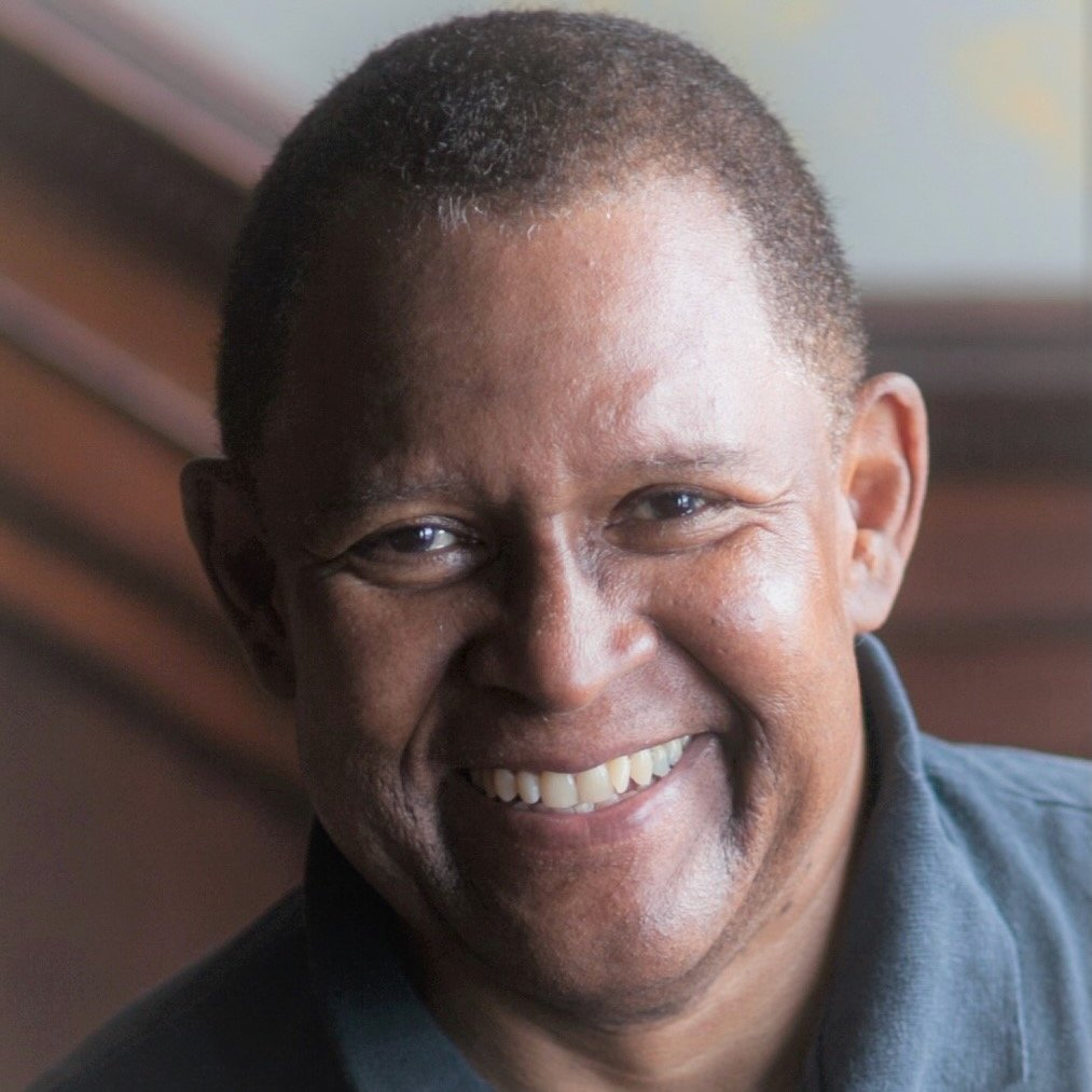 Portrait of a smiling man with short hair, wearing a dark shirt, indoors.