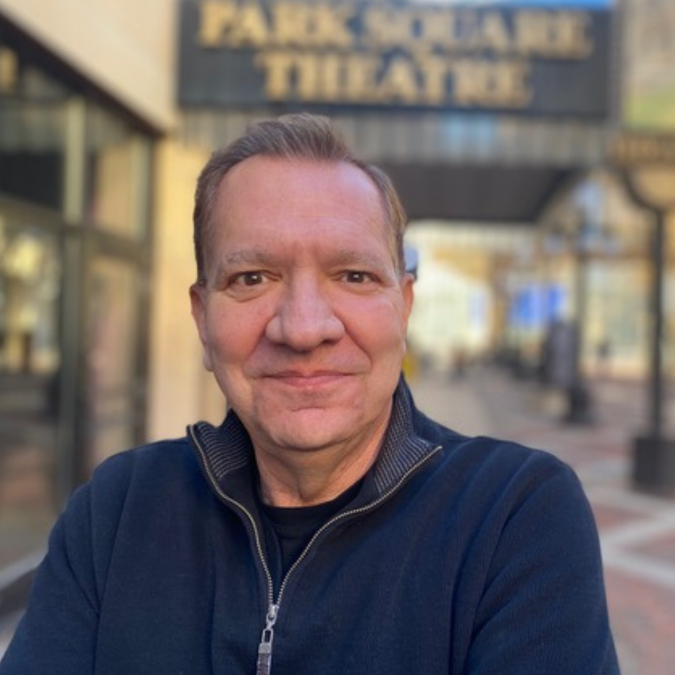 A man smiling outside of a theater titled 'Theatre Tihany' in the background
