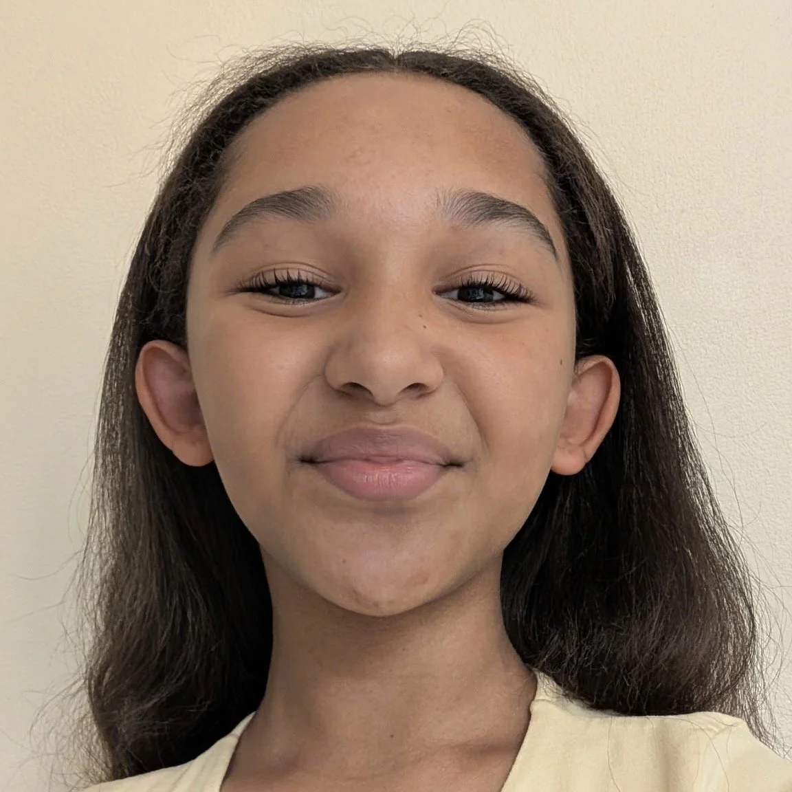 Close-up of a young girl with long dark hair, smiling softly, with a beige background.