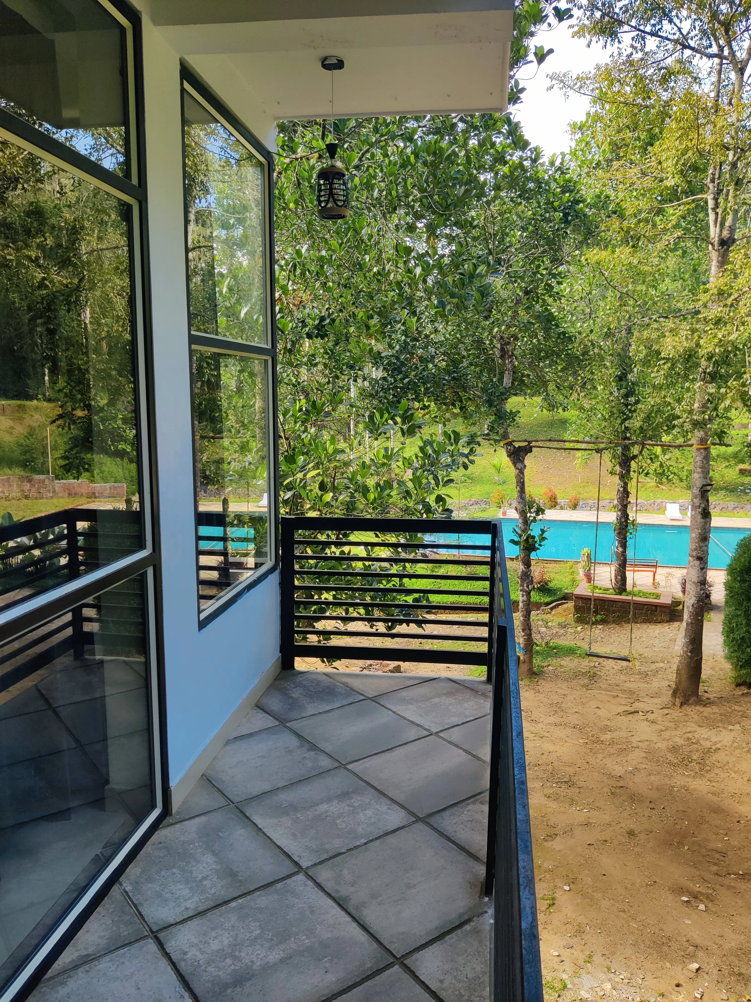 Balcony overlooking a backyard with trees and a swimming pool, with a hanging lantern near the ceiling.