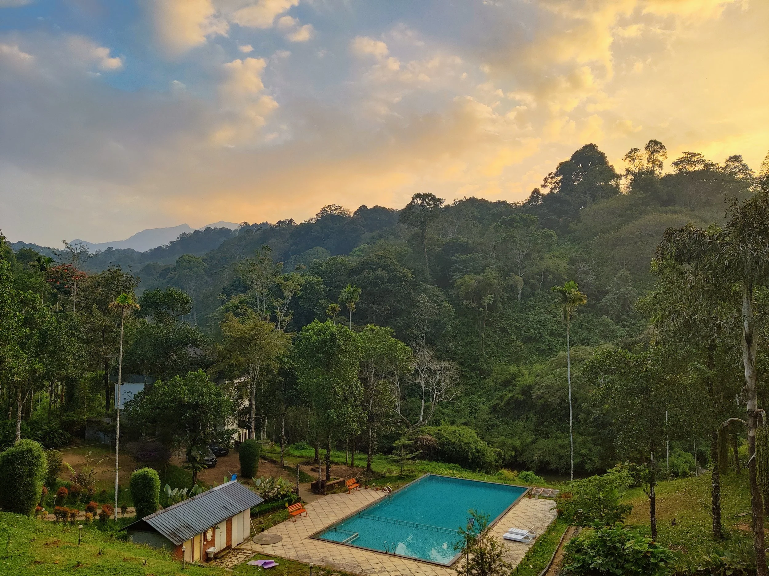 A mountain landscape at sunset with a swimming pool and lush greenery in the foreground.