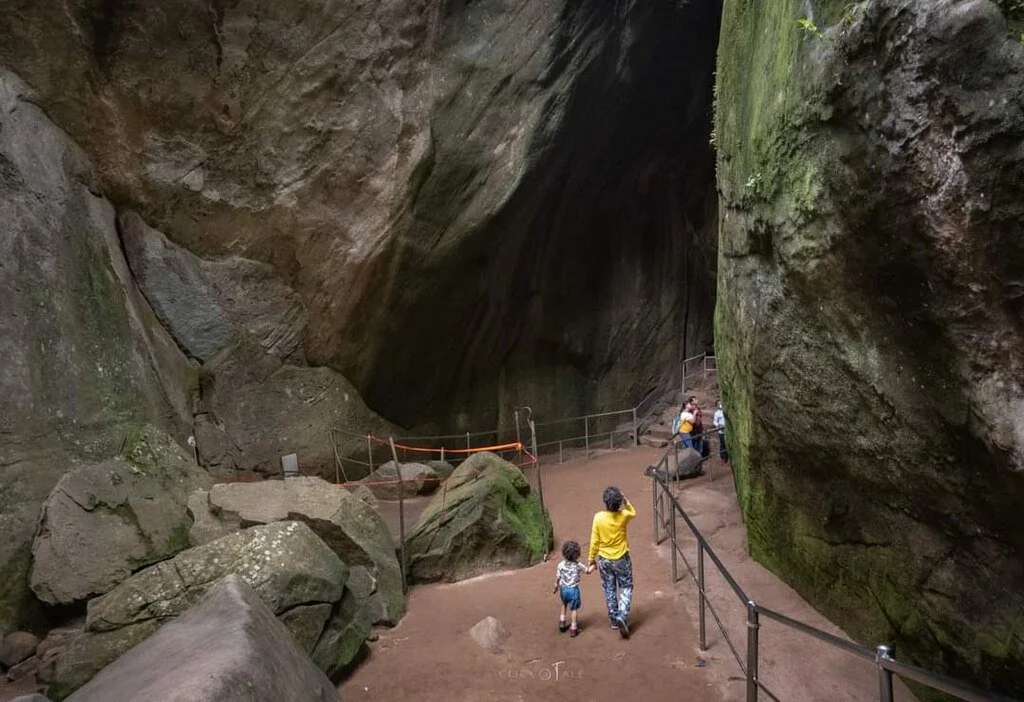 People walking along a path inside a large cave with moss-covered rock walls.