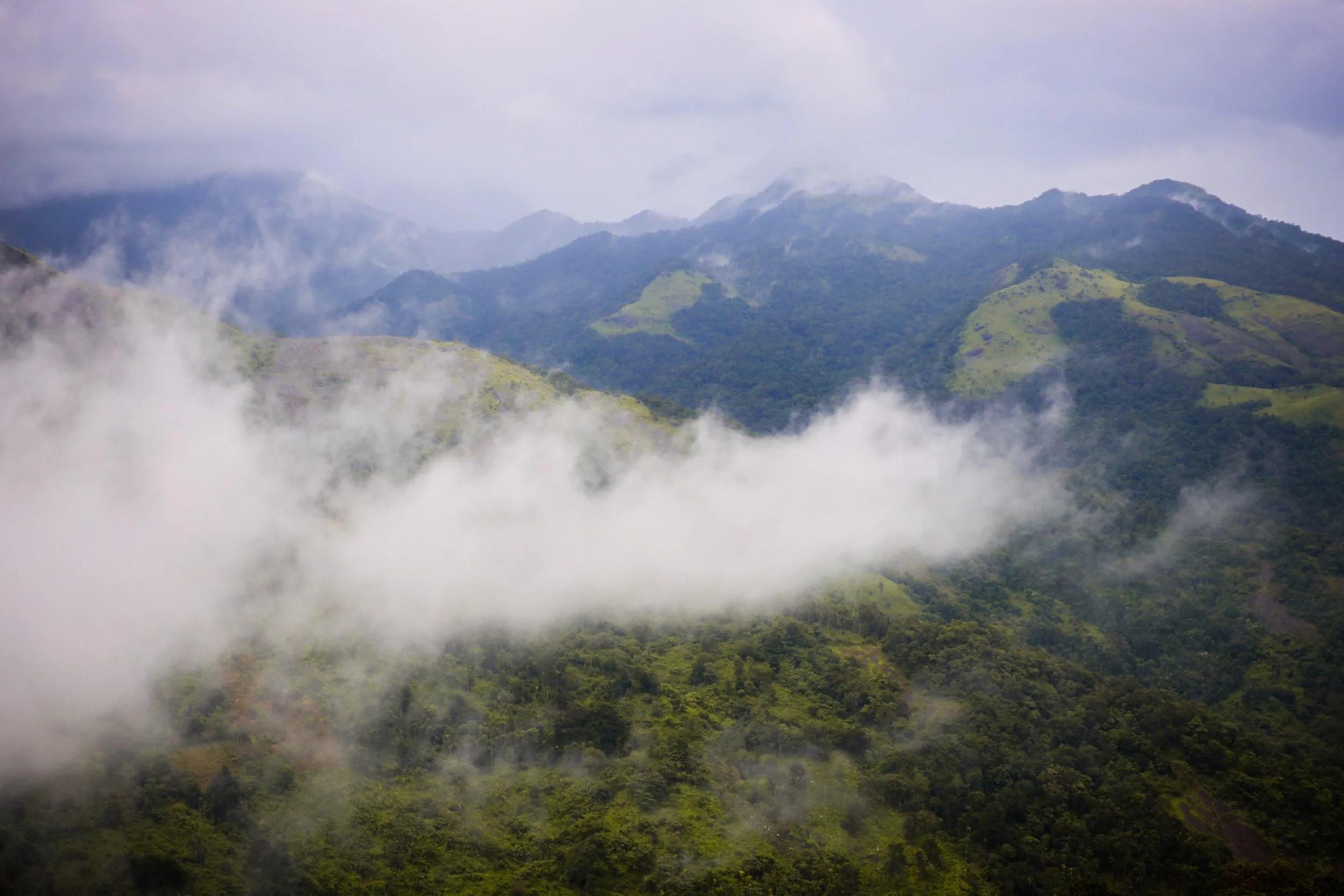 Mountain landscape with green hills, cloudy sky, and fog in the valleys.