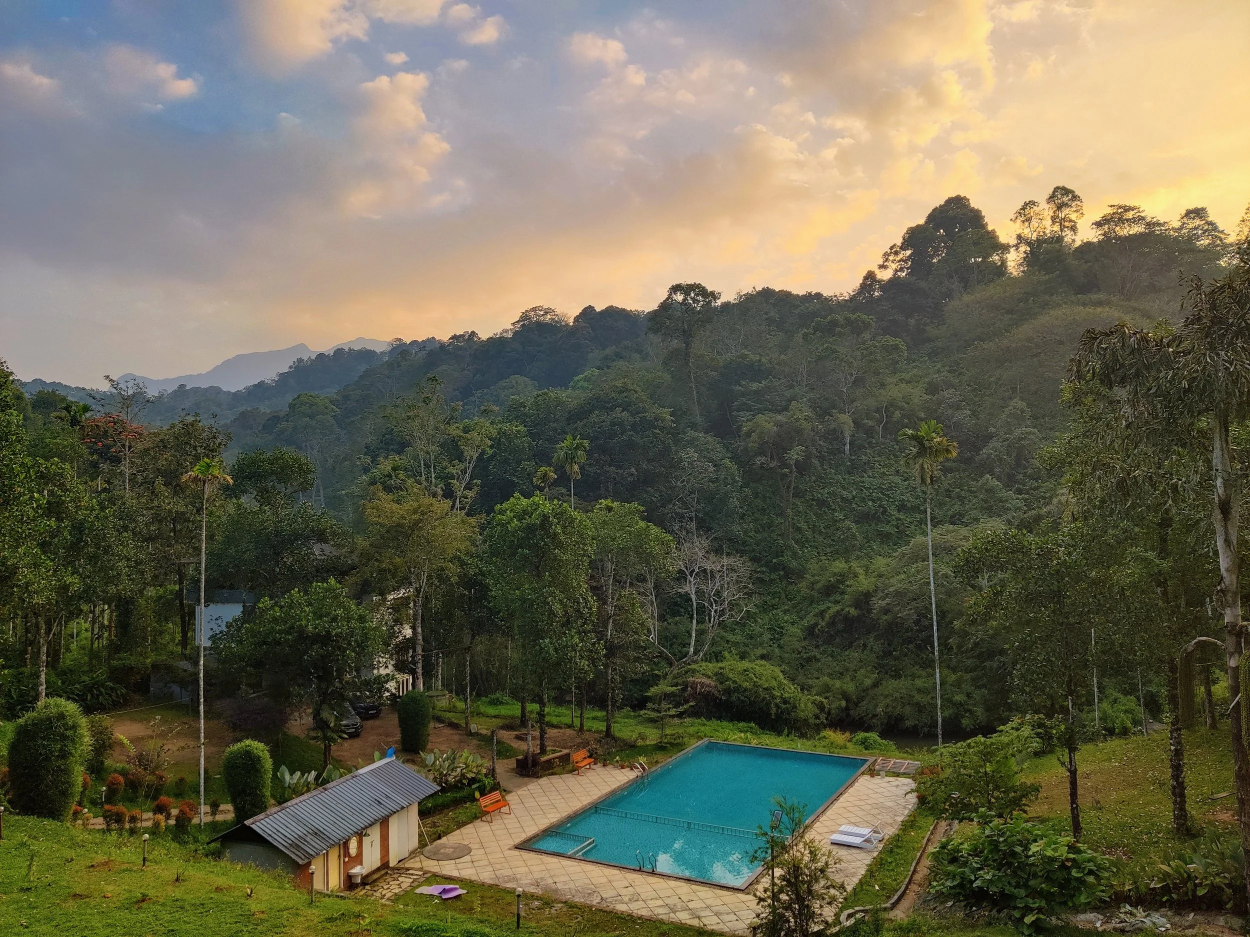 A scenic mountain landscape at sunset with a lush green forest and a swimming pool in the foreground.