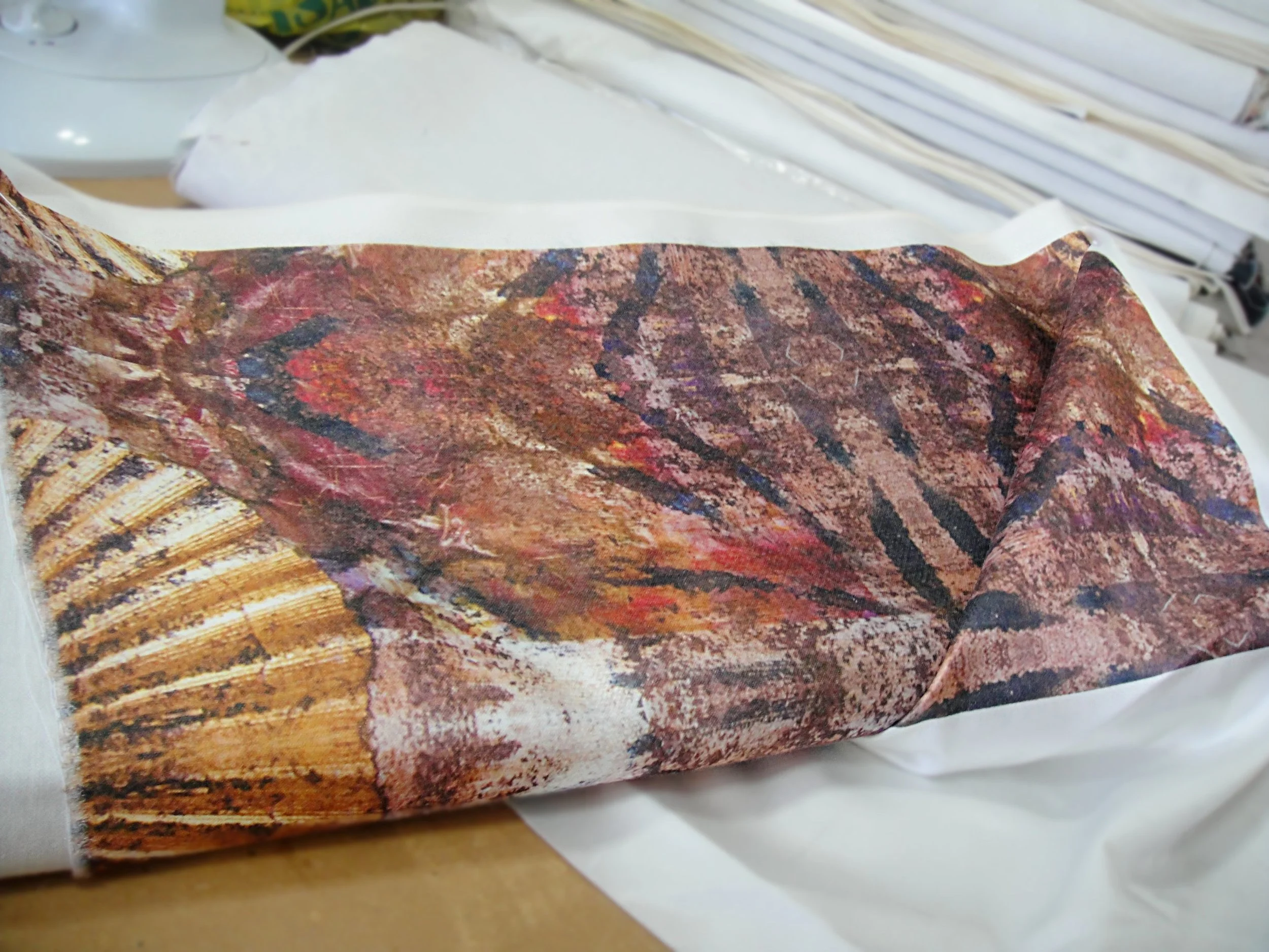 A close-up of a colorful folded fabric with a pattern in various shades of red, brown, black, and purple, resting on a white surface.