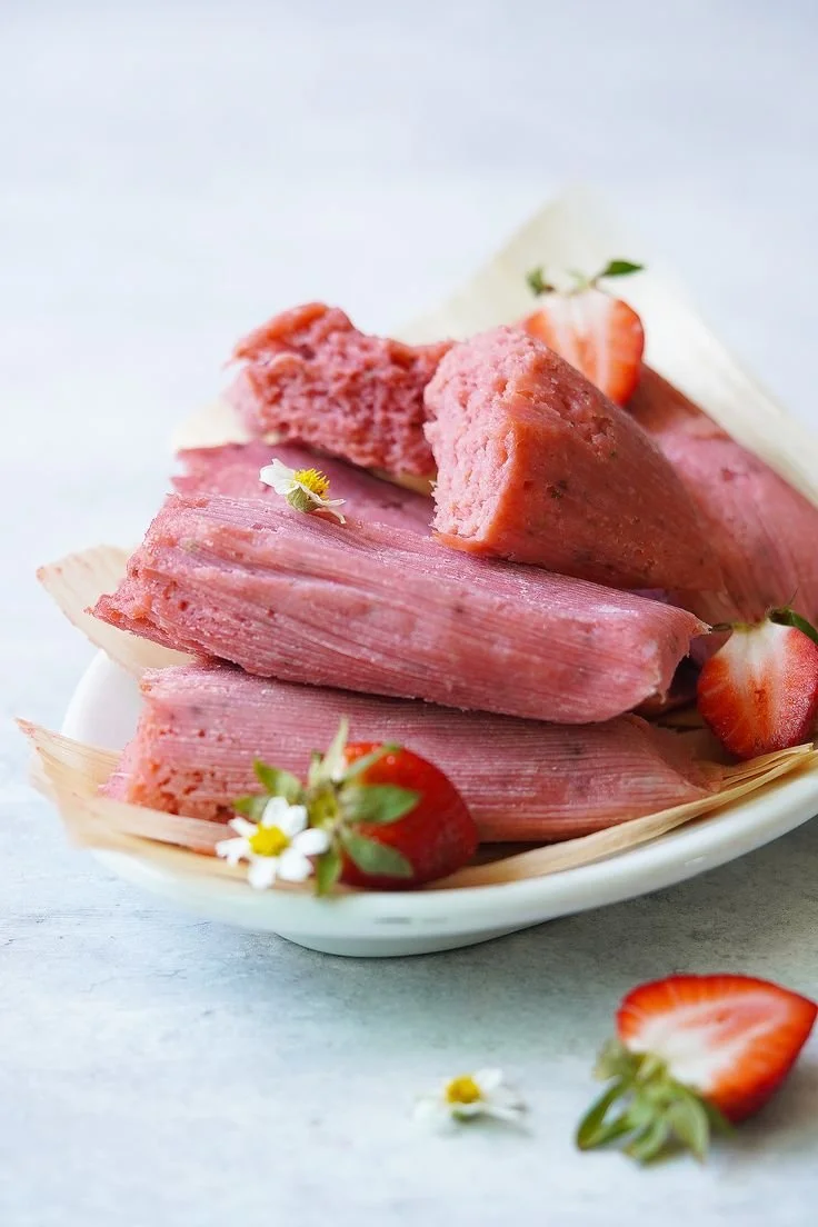 Slices of pink-hued ham with strawberries and small white flowers in a white dish.