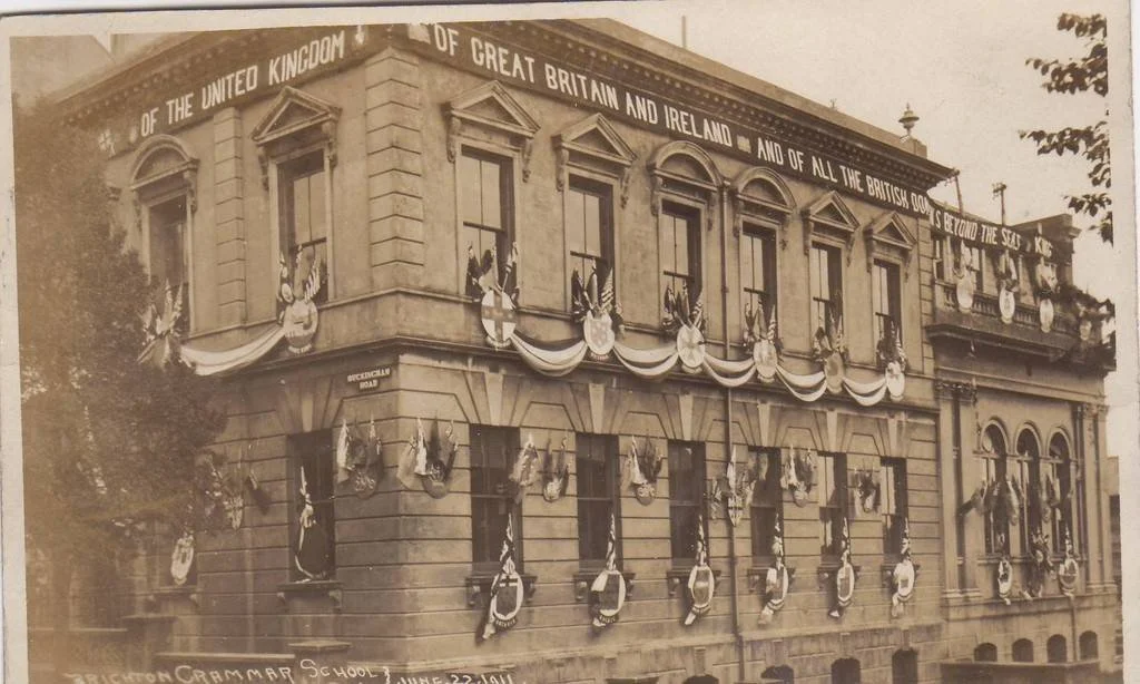 A three-storey old building decorated with cloth and shields, on a street corner.