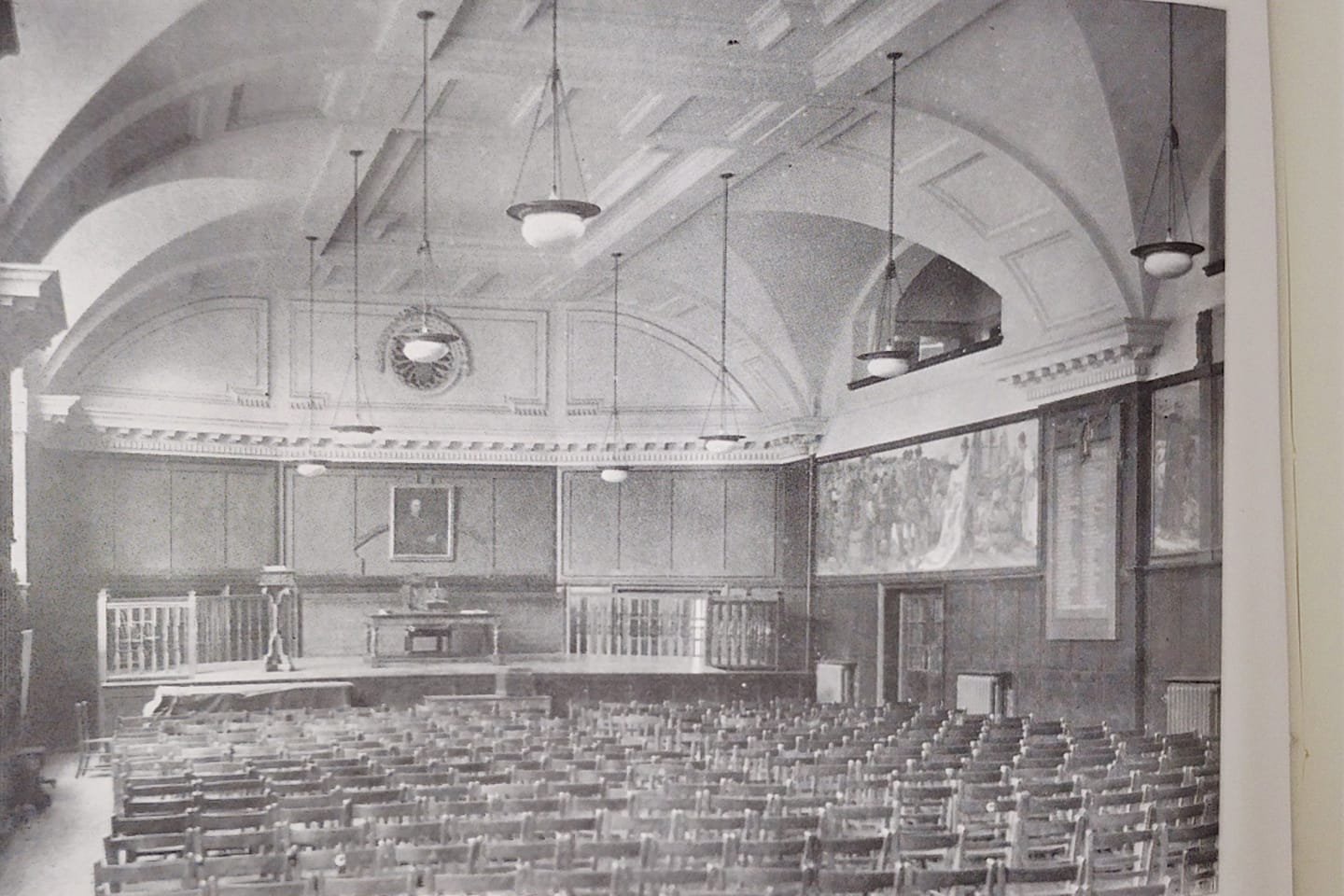 The BHASVIC Main Hall shortly after opening, with chairs filling the room, with the stage at the other side. Lights hang down and a large portrait hangs at the far side.