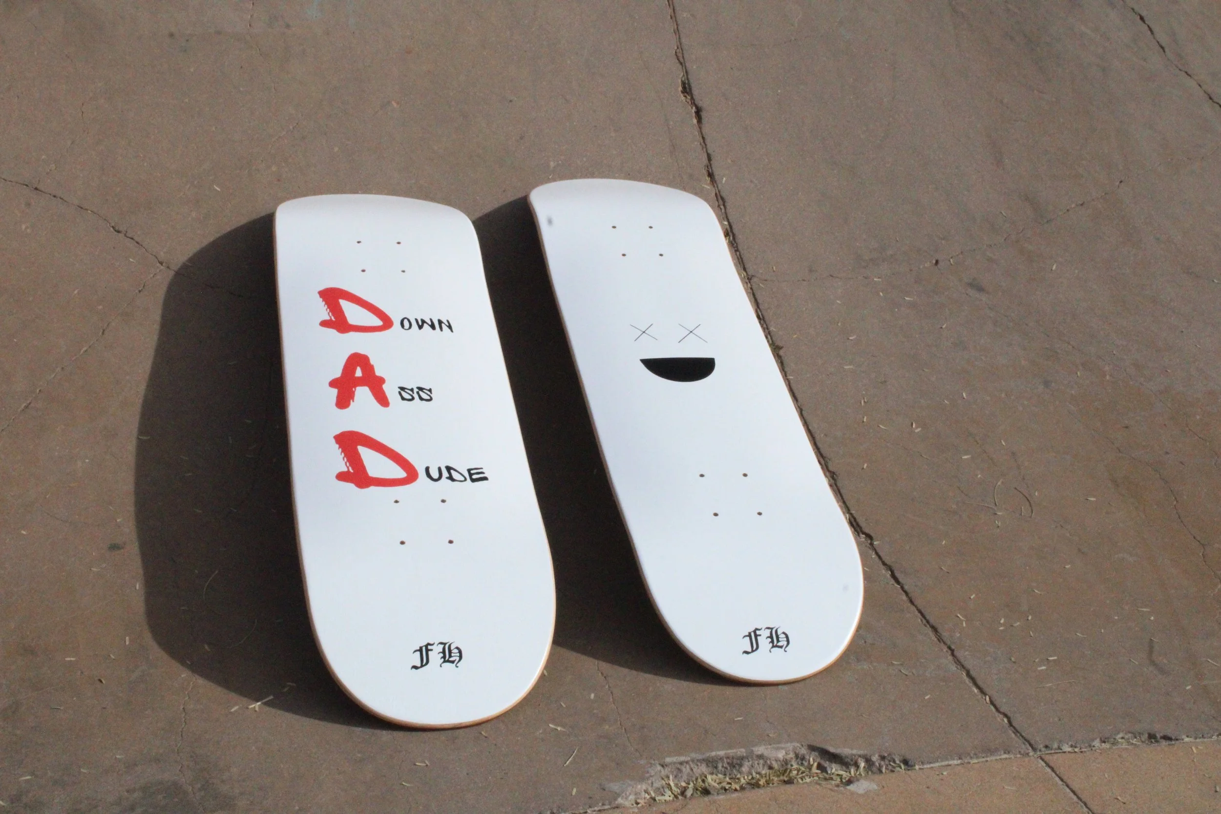 Two skateboards lying on the ground; one with the word 'DADDY' and the other with a smiling face with X's for eyes.