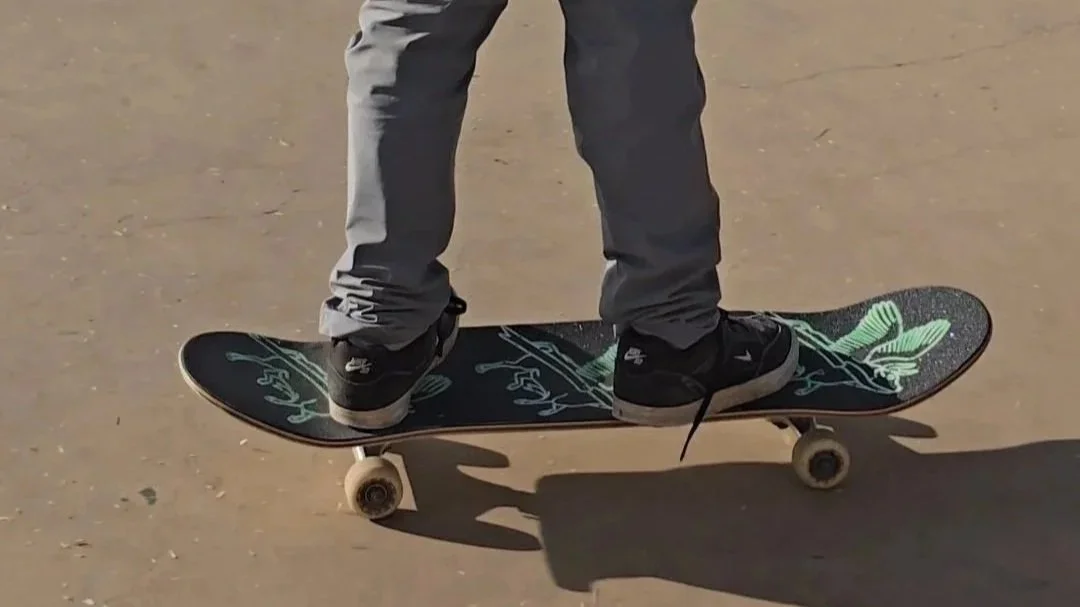 Close-up of a person riding a skateboard on a paved surface, wearing black shoes and gray pants.