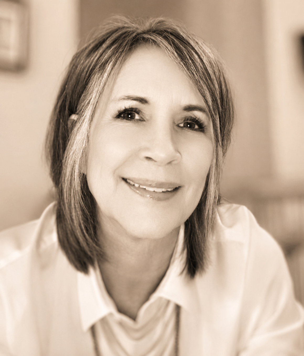 A woman smiling with shoulder-length hair wearing a light-colored collared shirt.