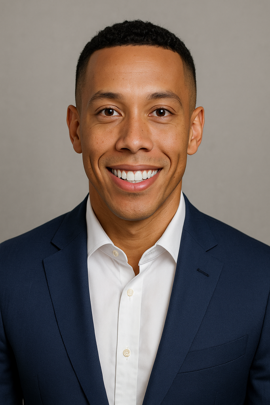 Headshot of a young man with short dark hair, smiling, wearing a navy blue suit and white dress shirt, against a neutral background.