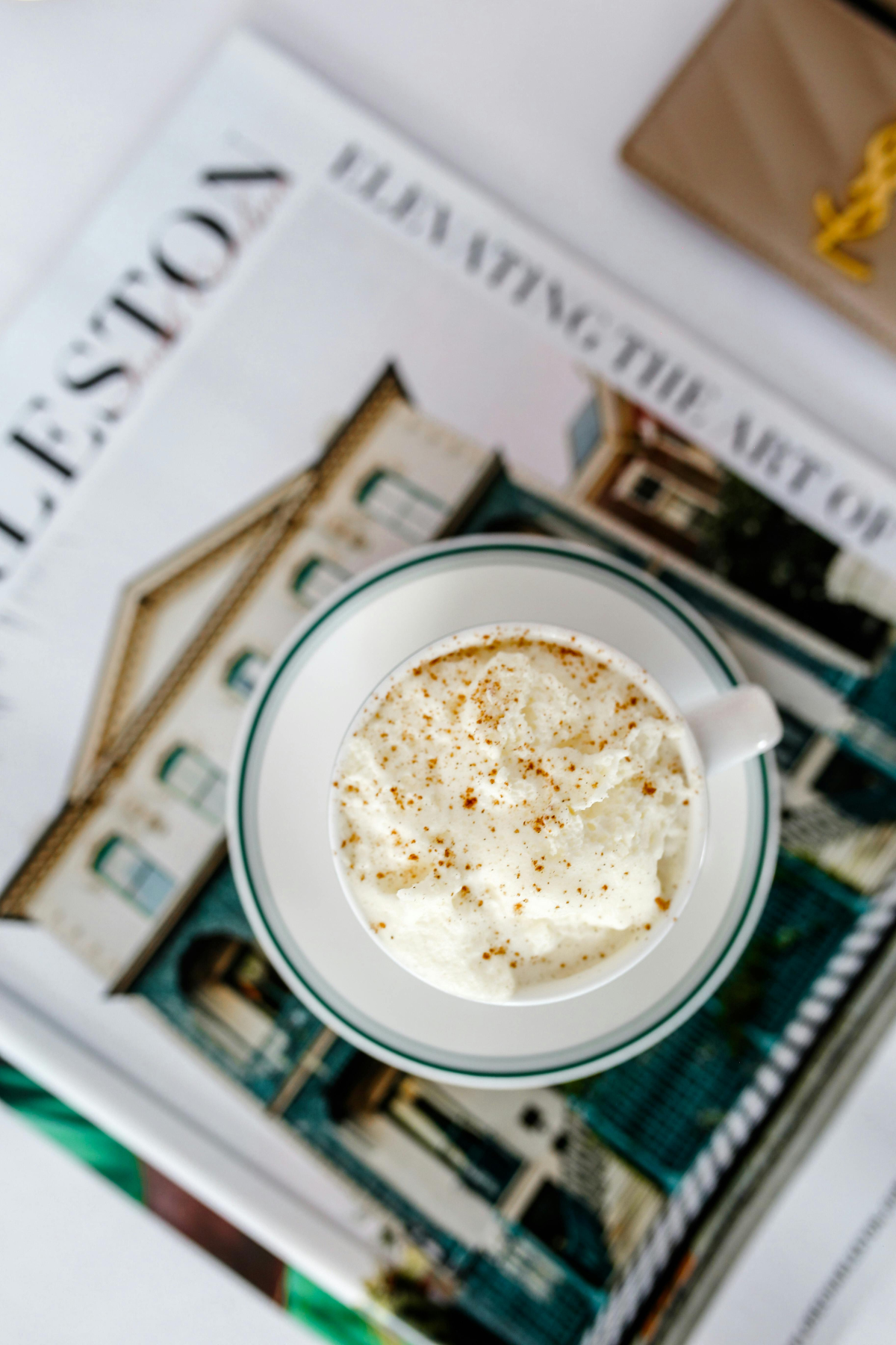 A mug of whipped cream-topped hot chocolate on top of a magazine about Charleston real estate.