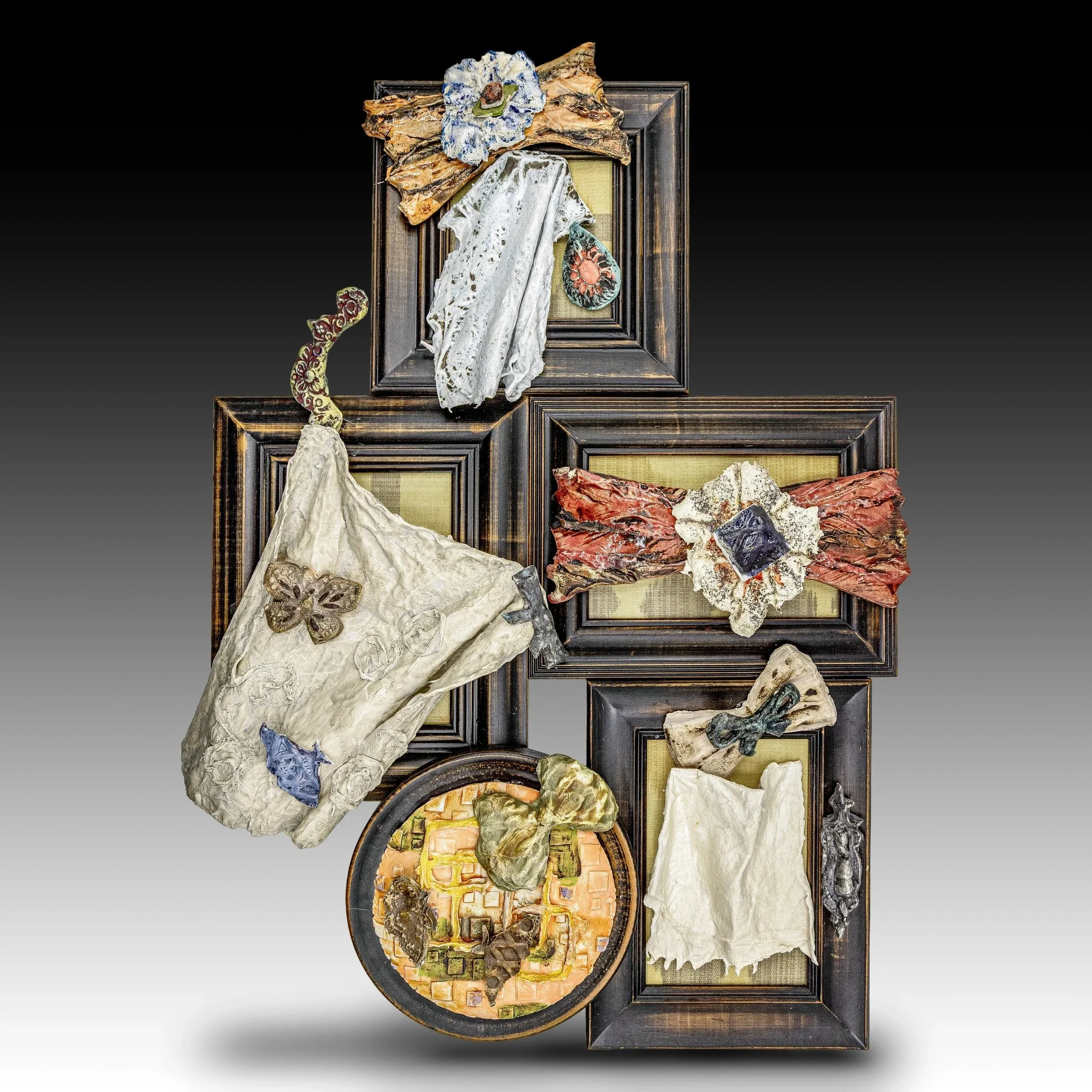 Mixed media artwork display with framed fabric pieces, textured paper, and small sculptures arranged in a collage style on a black gradient background.
