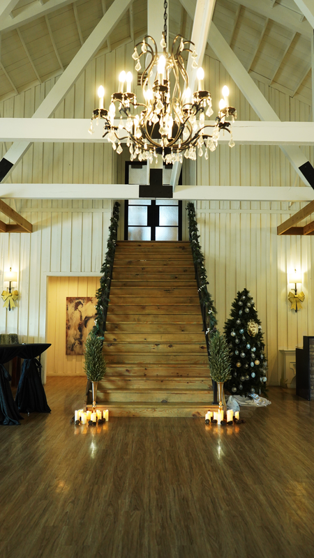 Interior of a rustic venue decorated for Christmas with a wooden staircase, a Christmas tree, candles, and a chandelier.