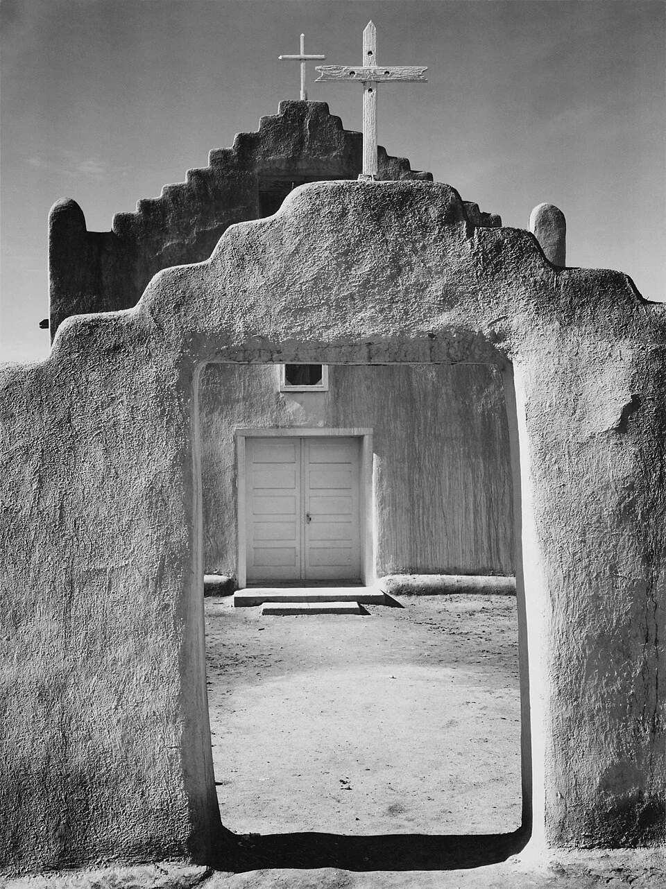 Ansel Adams black and white photograph of the Church at Taos Pueblo (1942). Adobe entrance and plaza architecture. Public domain image from National Archives.