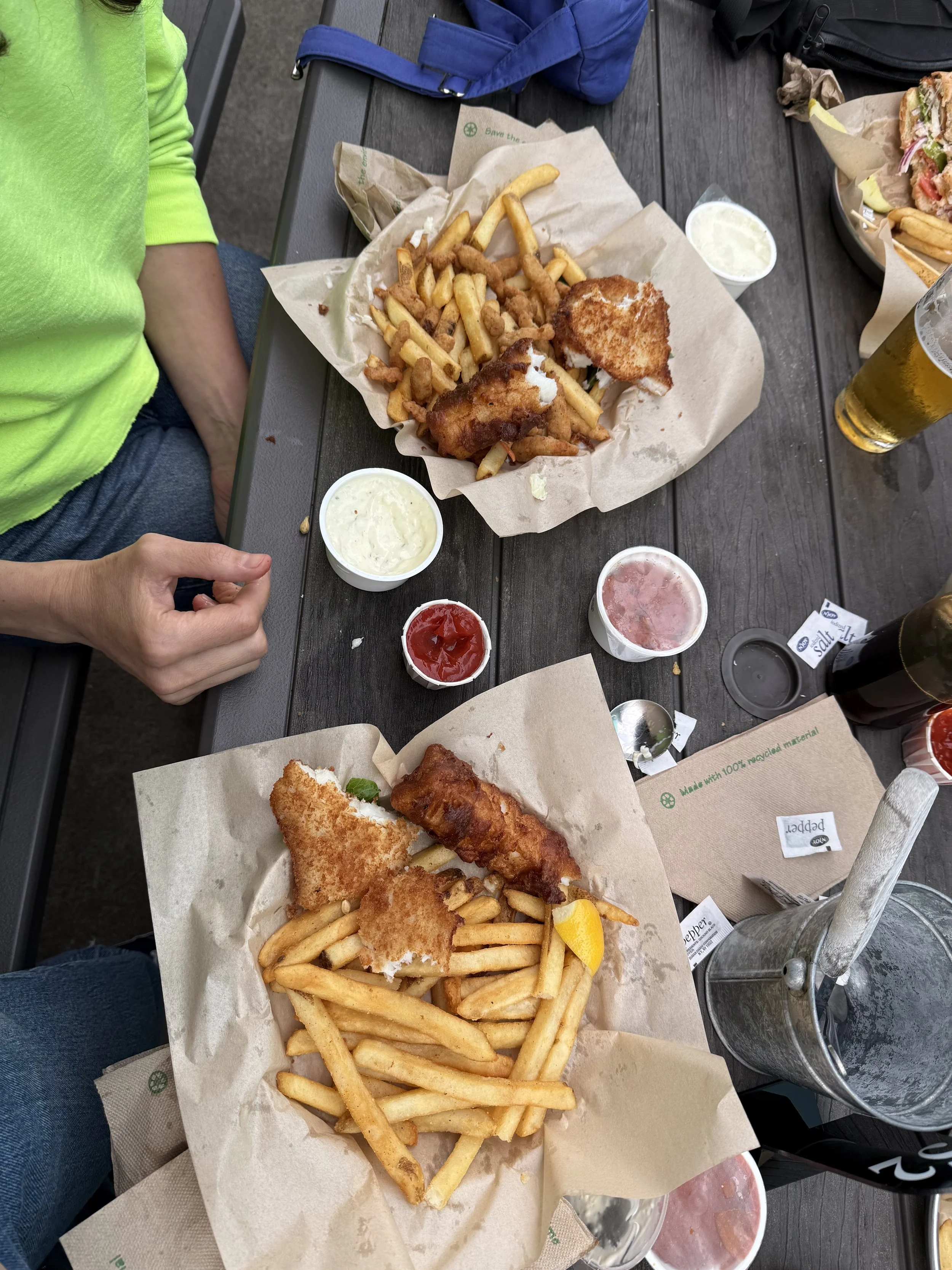 Fried fish and chips with French fries, served with tartar sauce, ketchup, and pink sauce on a wooden table.