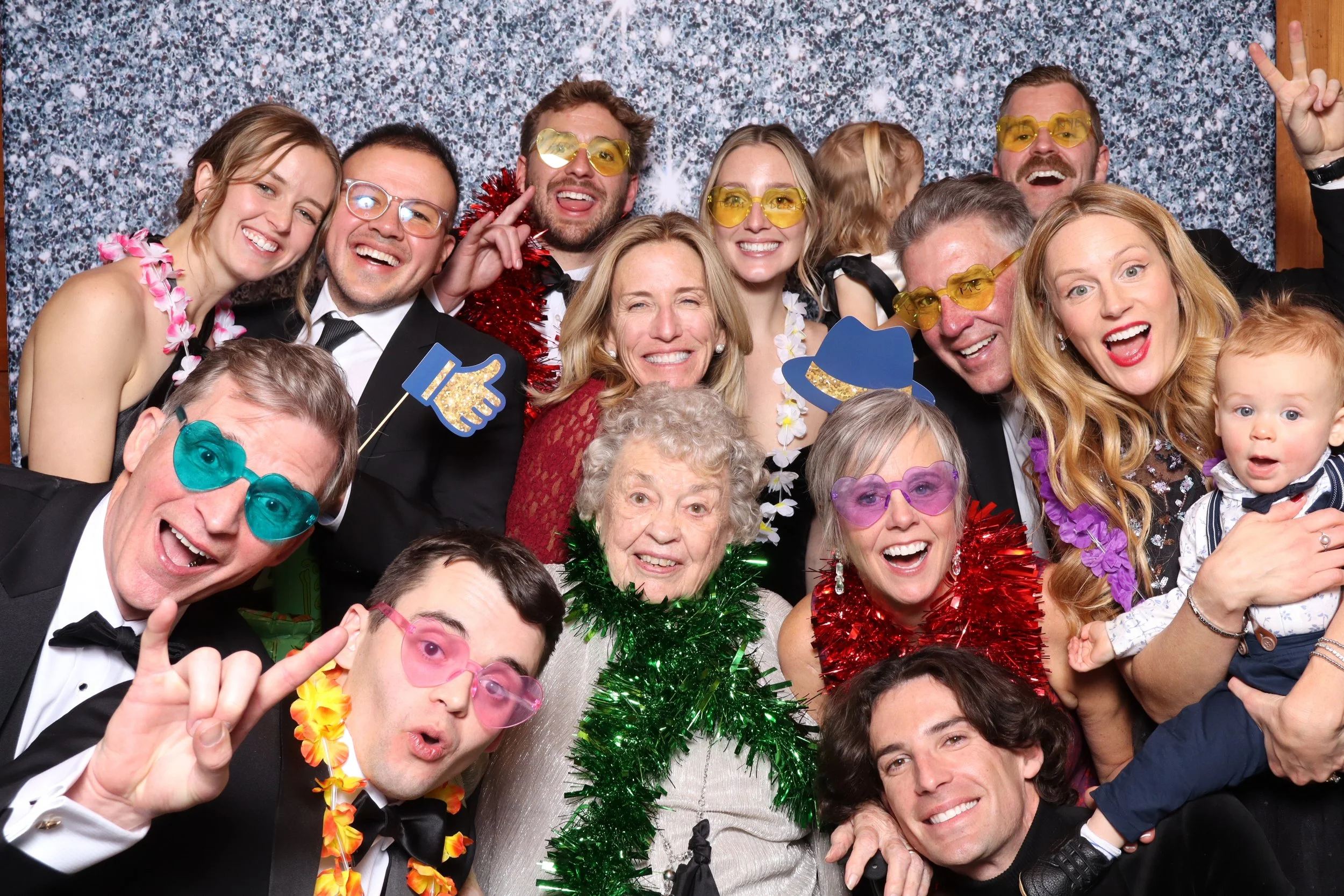 A group of people at a celebration, dressed in formal attire with colorful accessories, in front of a party backdrop.