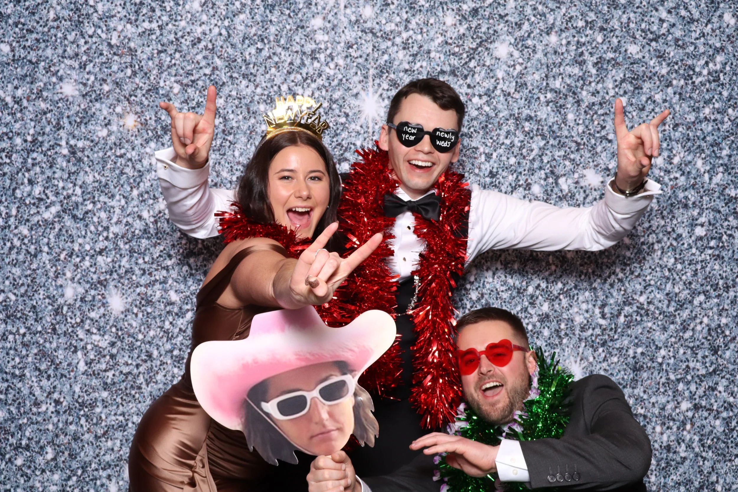 Groups of four friends celebrating New Year's Eve in party attire with festive decorations, against a silver glittery backdrop.