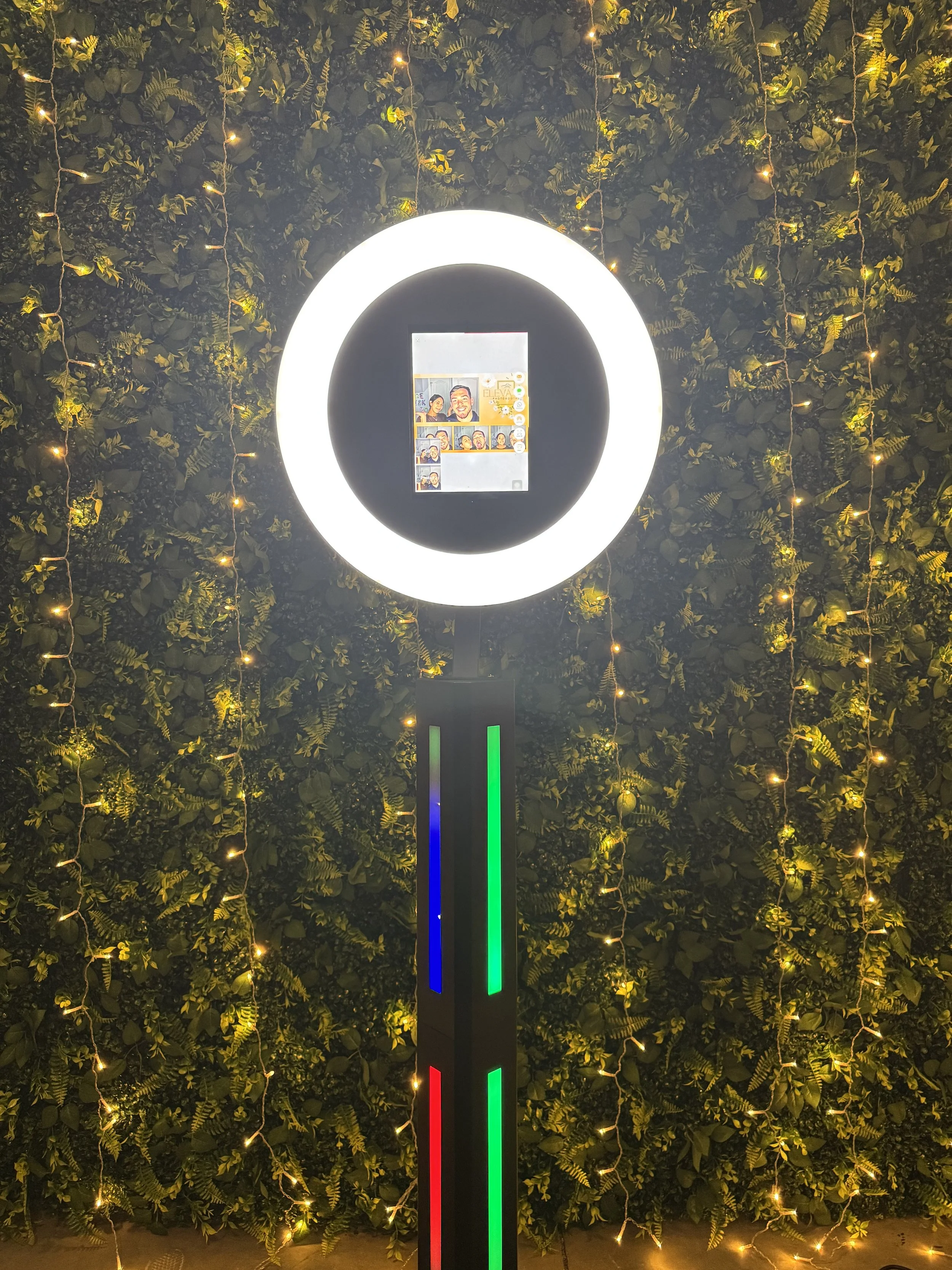 A black photobooth with circular lighting, placed on a red carpet, in front of a shimmering, sequined backdrop at an event.