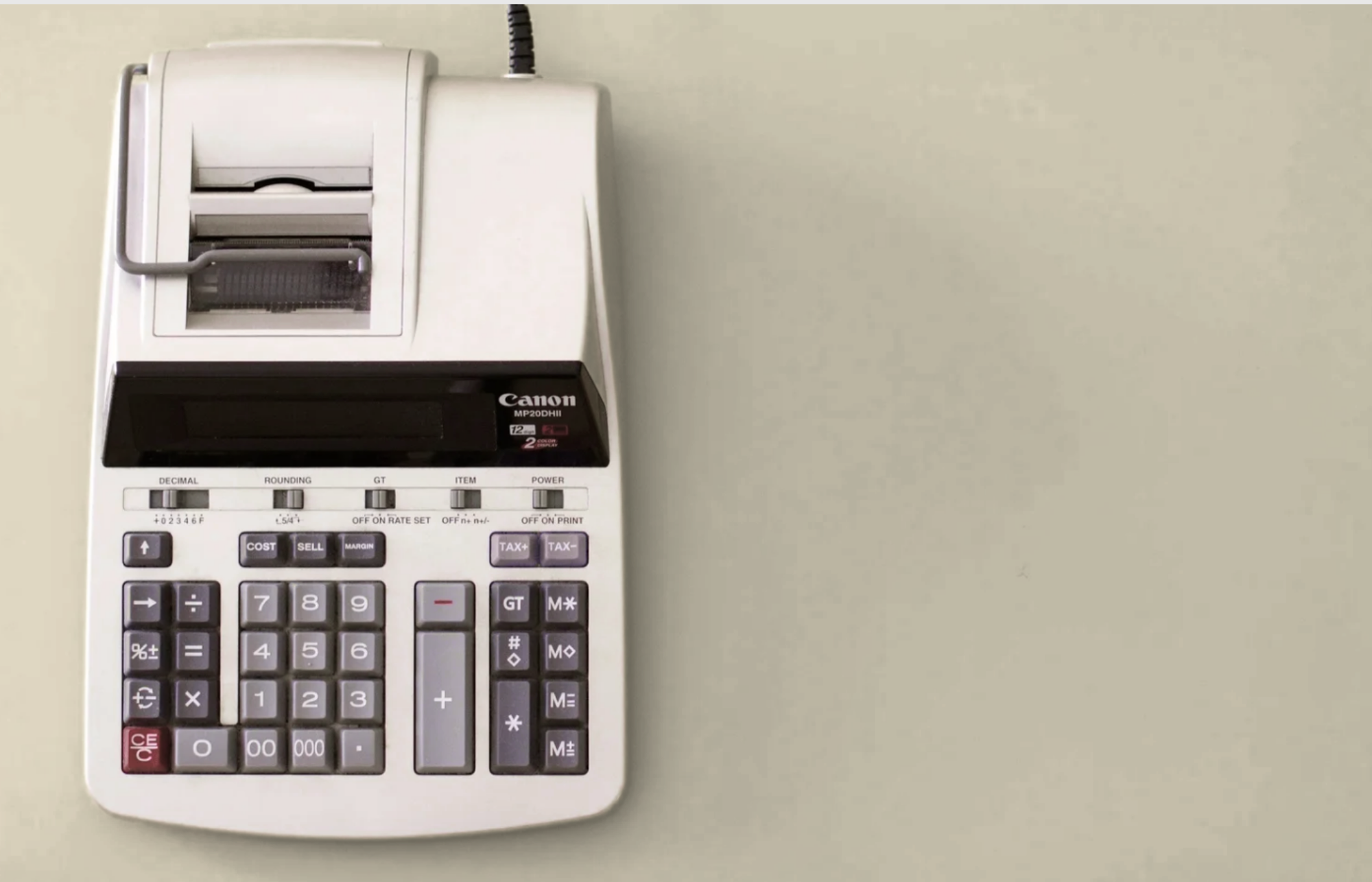 A white Canon calculator with printing capability and a built-in receipt tape, placed on a beige surface.