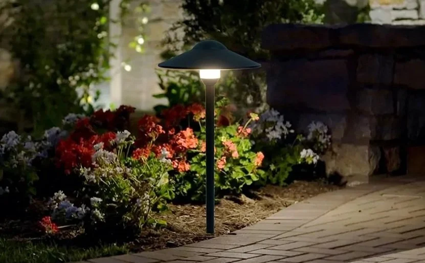 Garden pathway with pathway light illuminating colorful flowers and a stone wall at night.