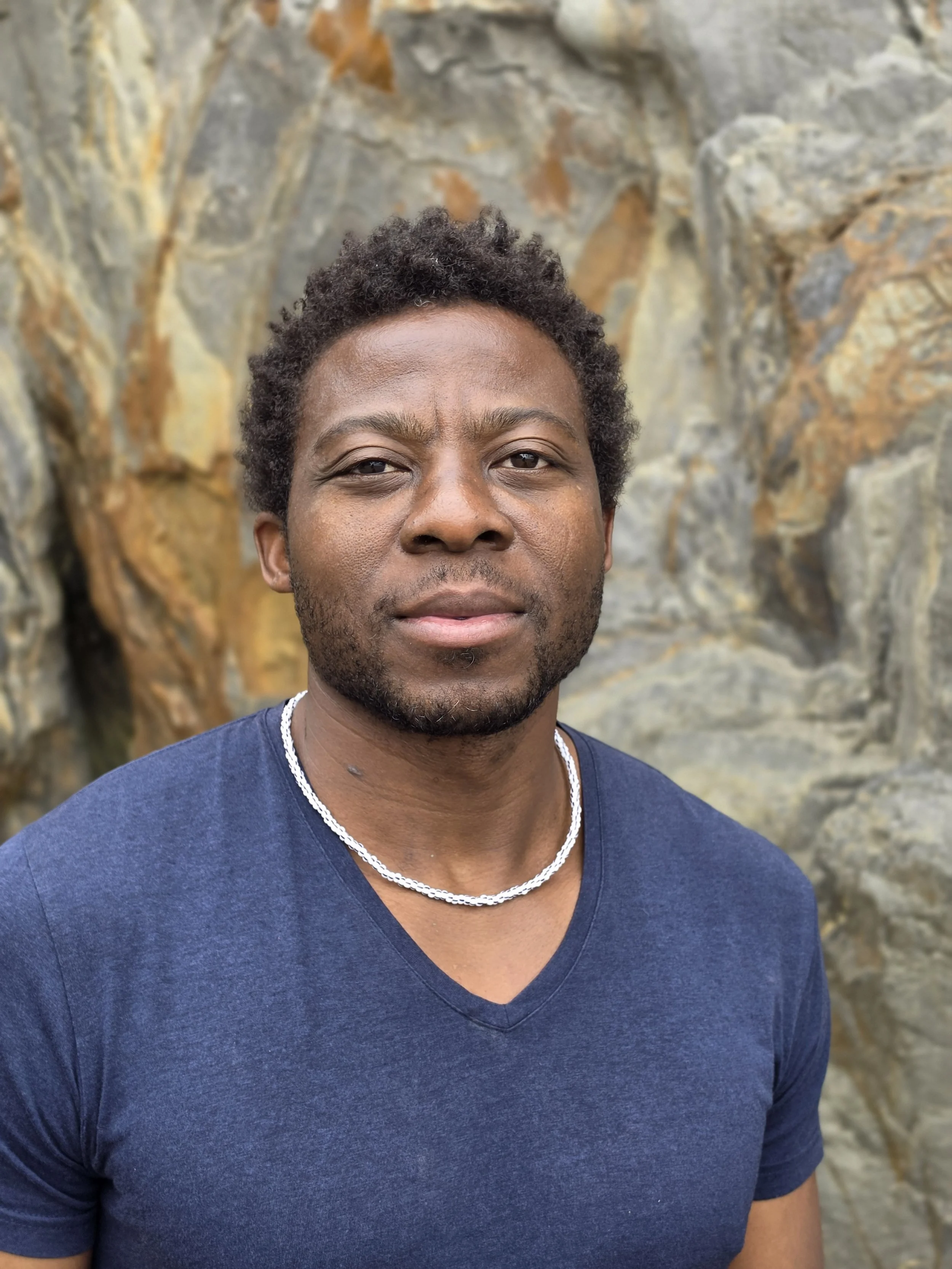 Headshot of man in blue shirt with white necklace