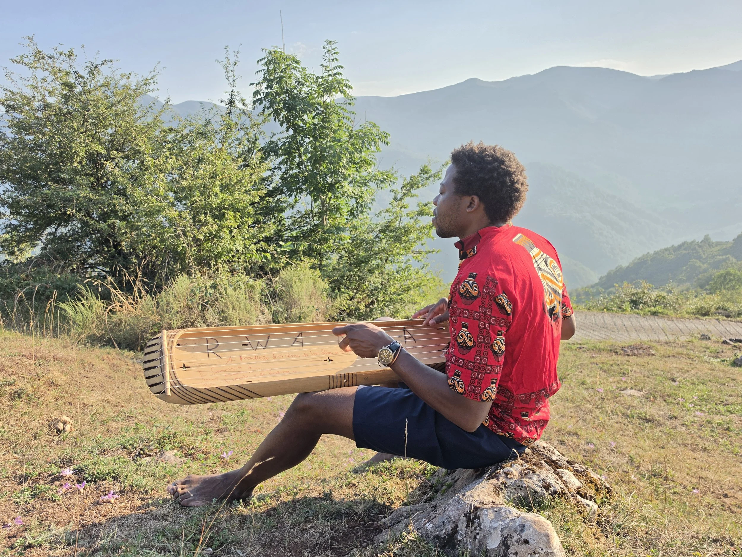 Man playing an inanga in front of a mountain rainge