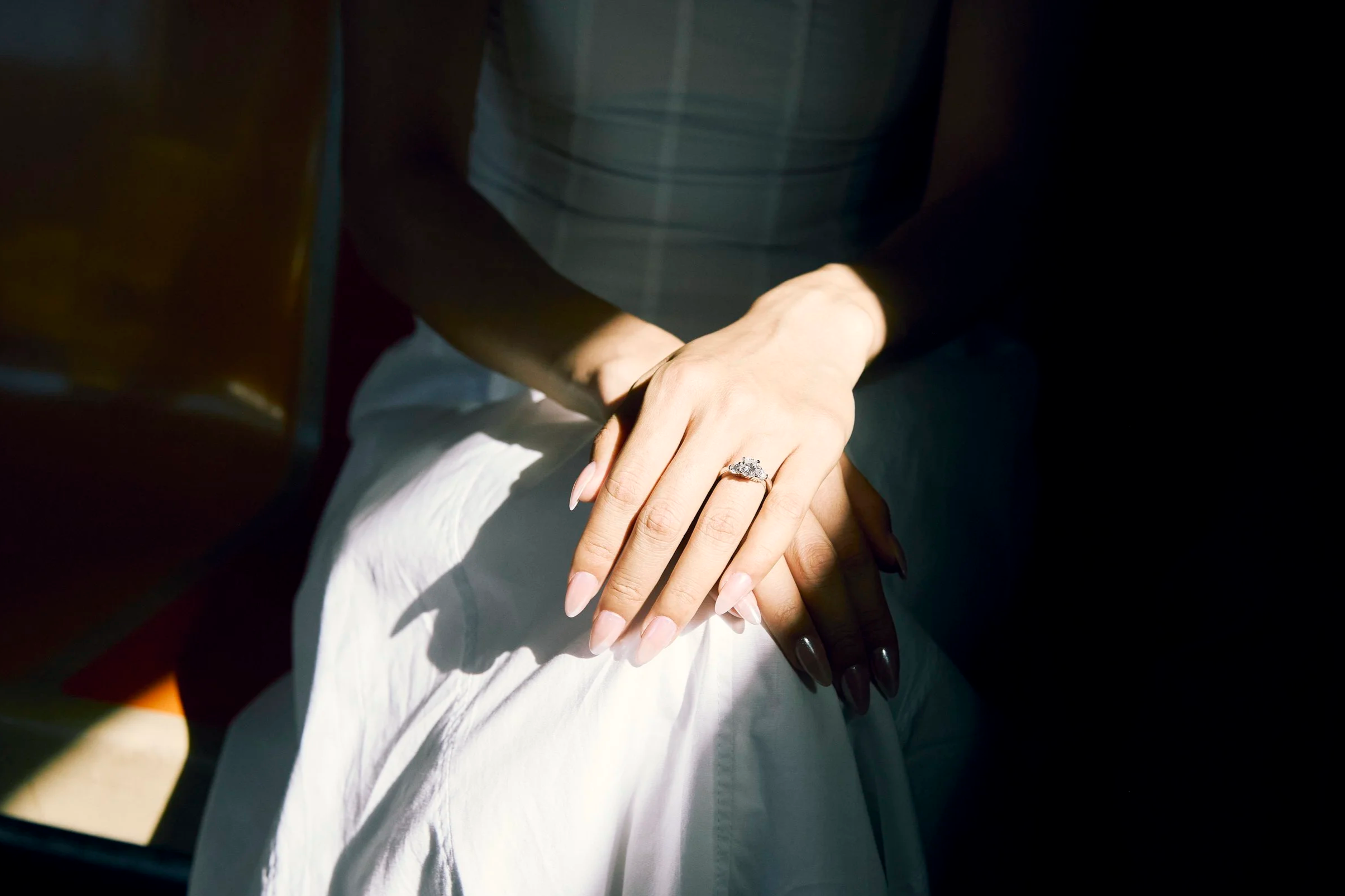 Close-up of a woman's hand wearing an engagement ring, resting on another person's hand, with sunlight casting shadows.