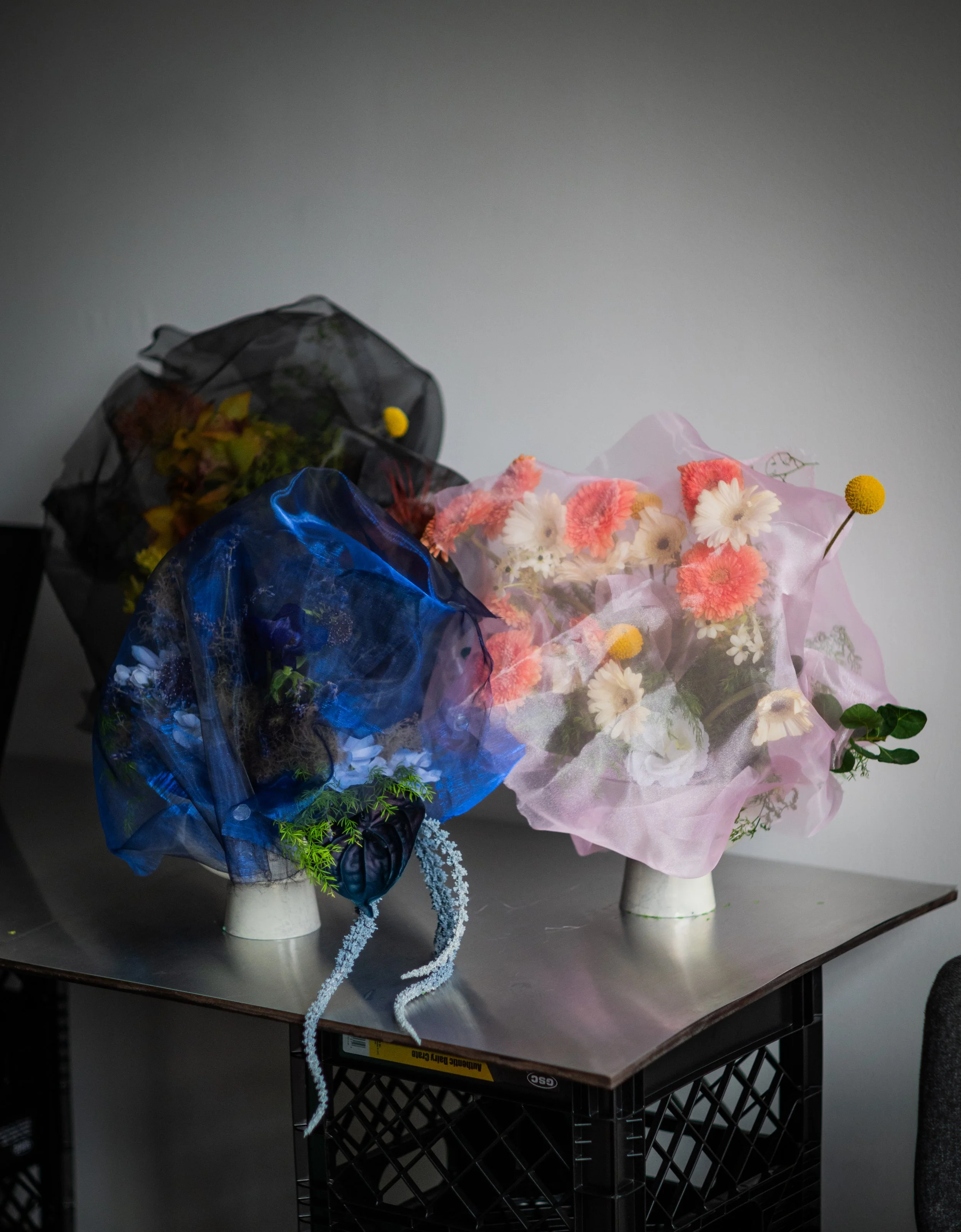 Multiple bouquets of flowers wrapped in colorful paper and plastic, placed on a black metal table with a grey background.
