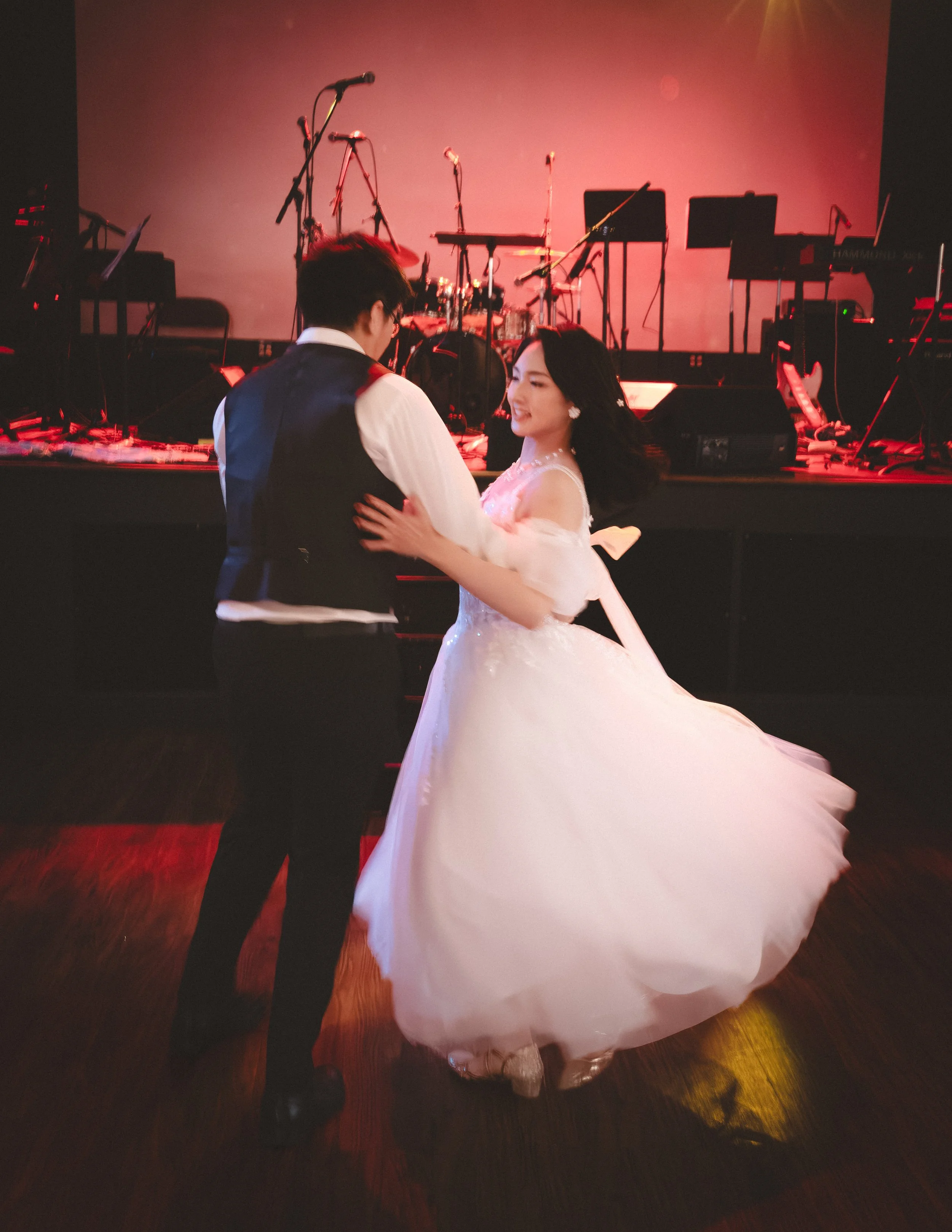 A couple dancing at a formal event with a stage and musical instruments in the background.