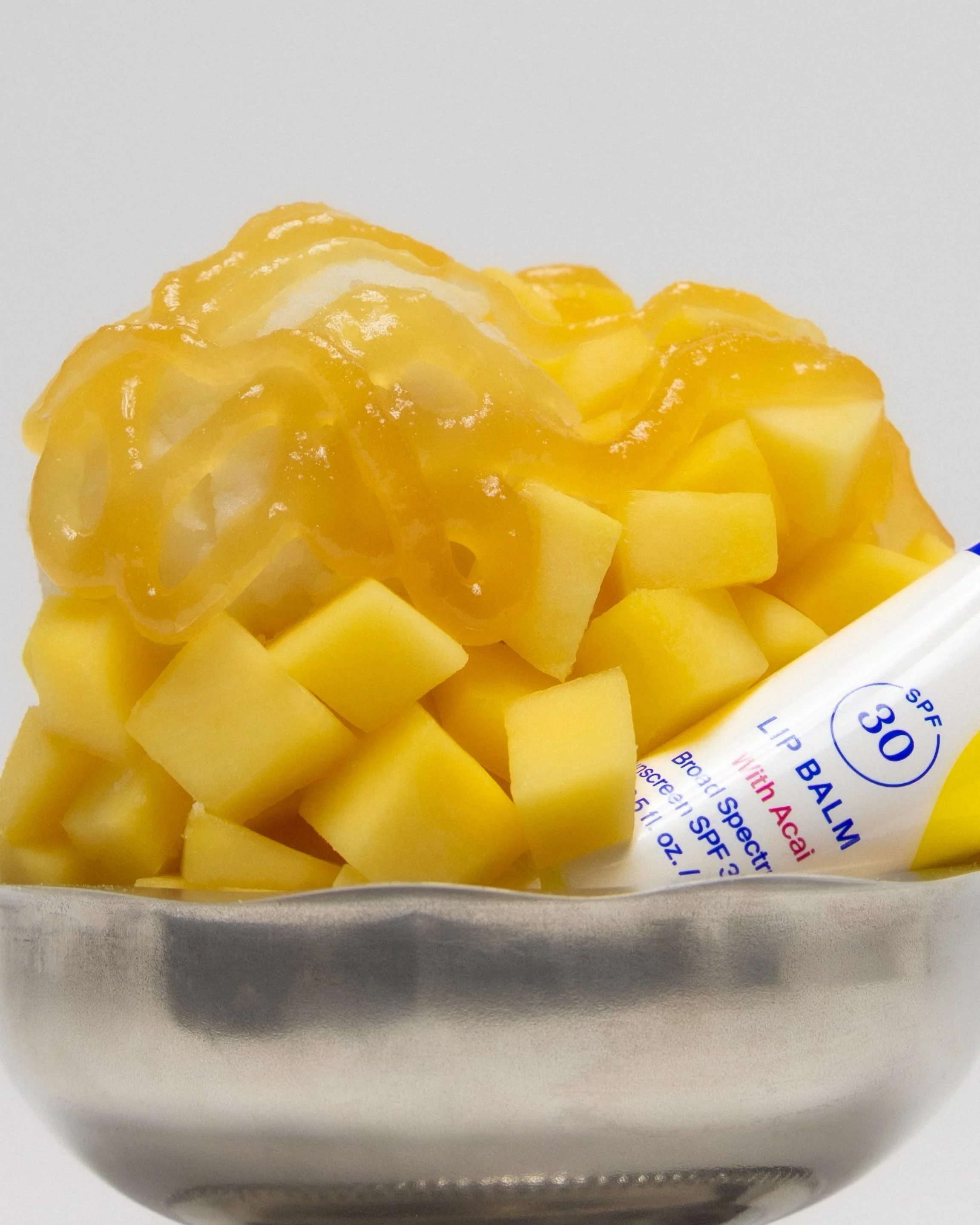 Close-up image of cubed, cooked, mangoes in a silver tray with a lip balm.