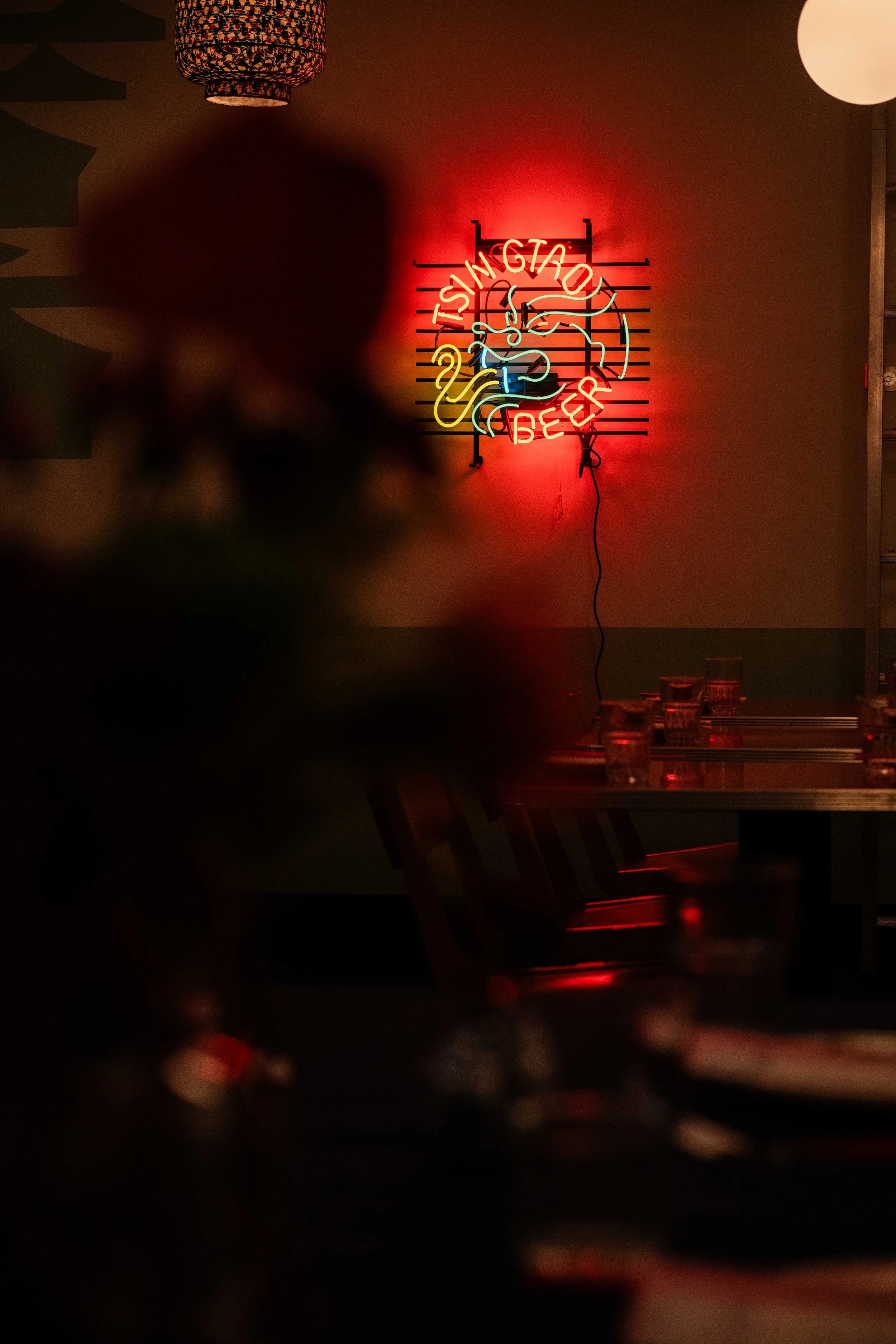A neon sign for a restaurant called 'Tsing Tao Beer' with a flaming dragon design, mounted on a beige wall in a dimly lit restaurant or bar.