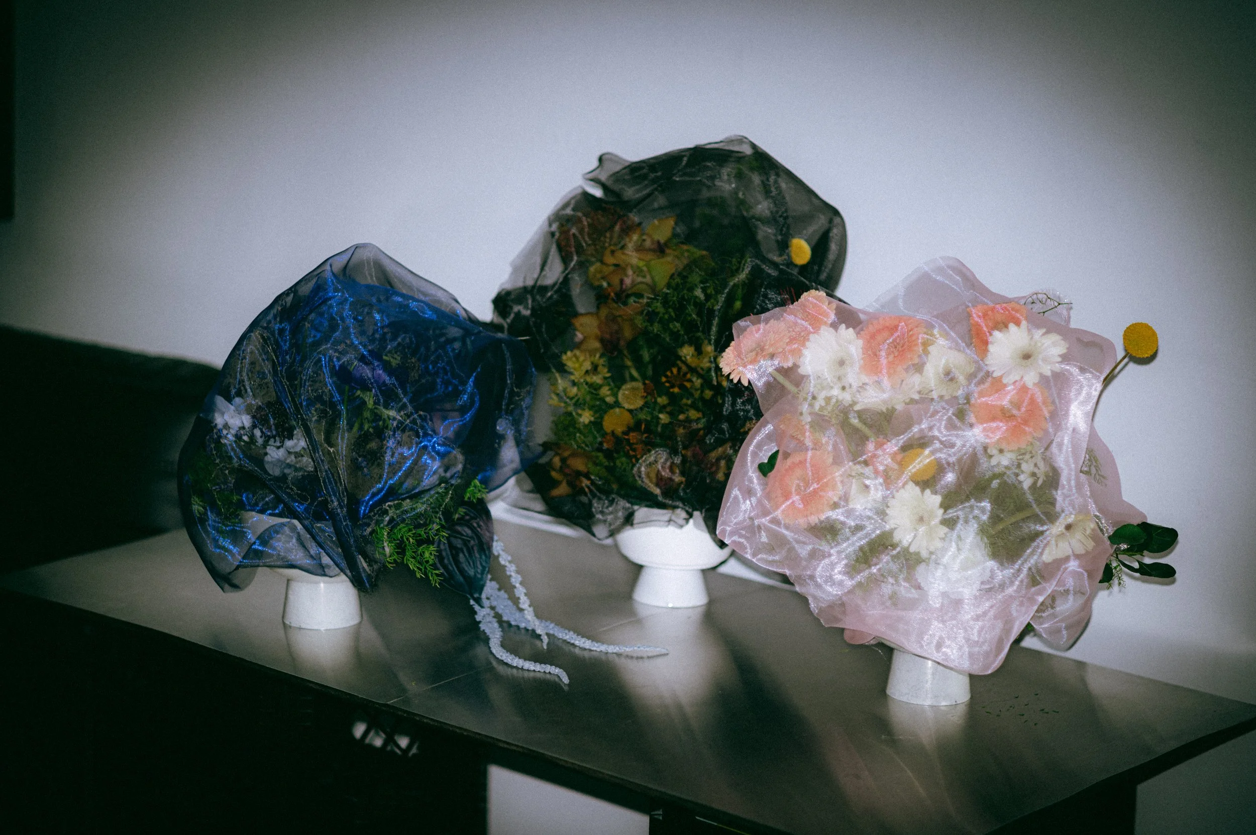 Arrangement of multiple floral bouquets on a table, wrapped in decorative paper and plastic, with some flowers including daisies visible.