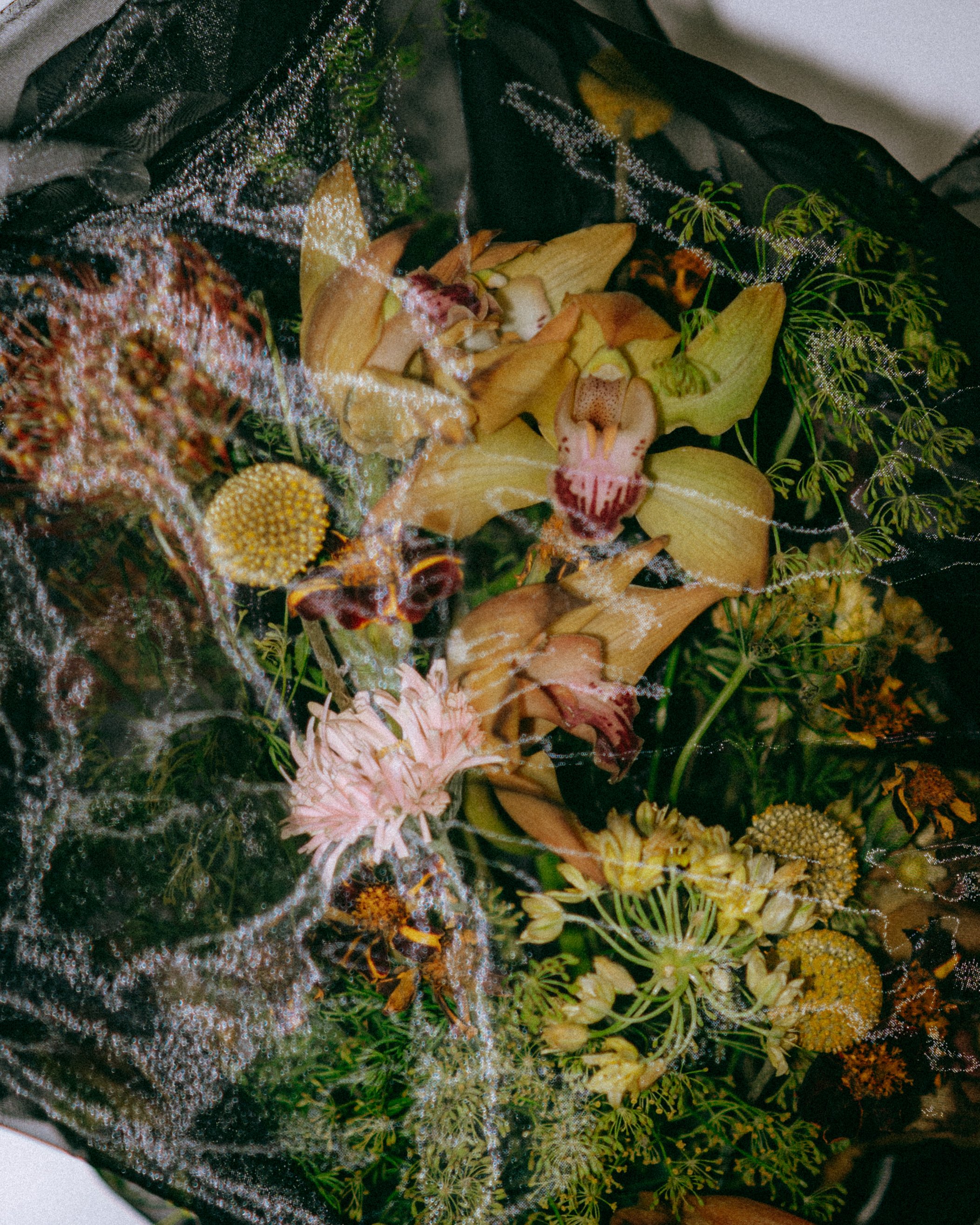 Close-up of a decorative floral arrangement with various flowers and greenery, wrapped in black tulle fabric.
